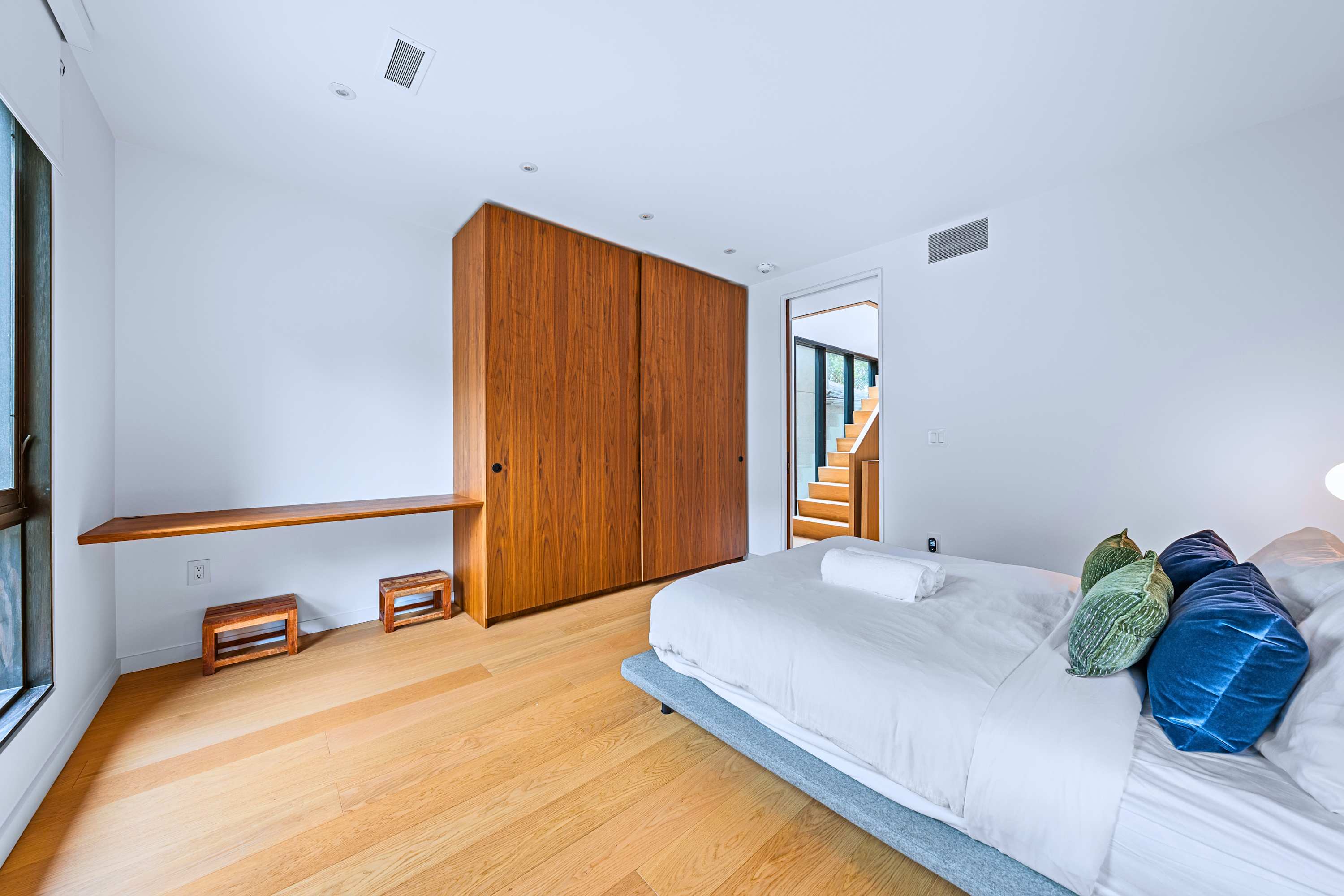 Spacious queen bedroom with floor-to-ceiling warm wood wardrobe and a multi-use nook.