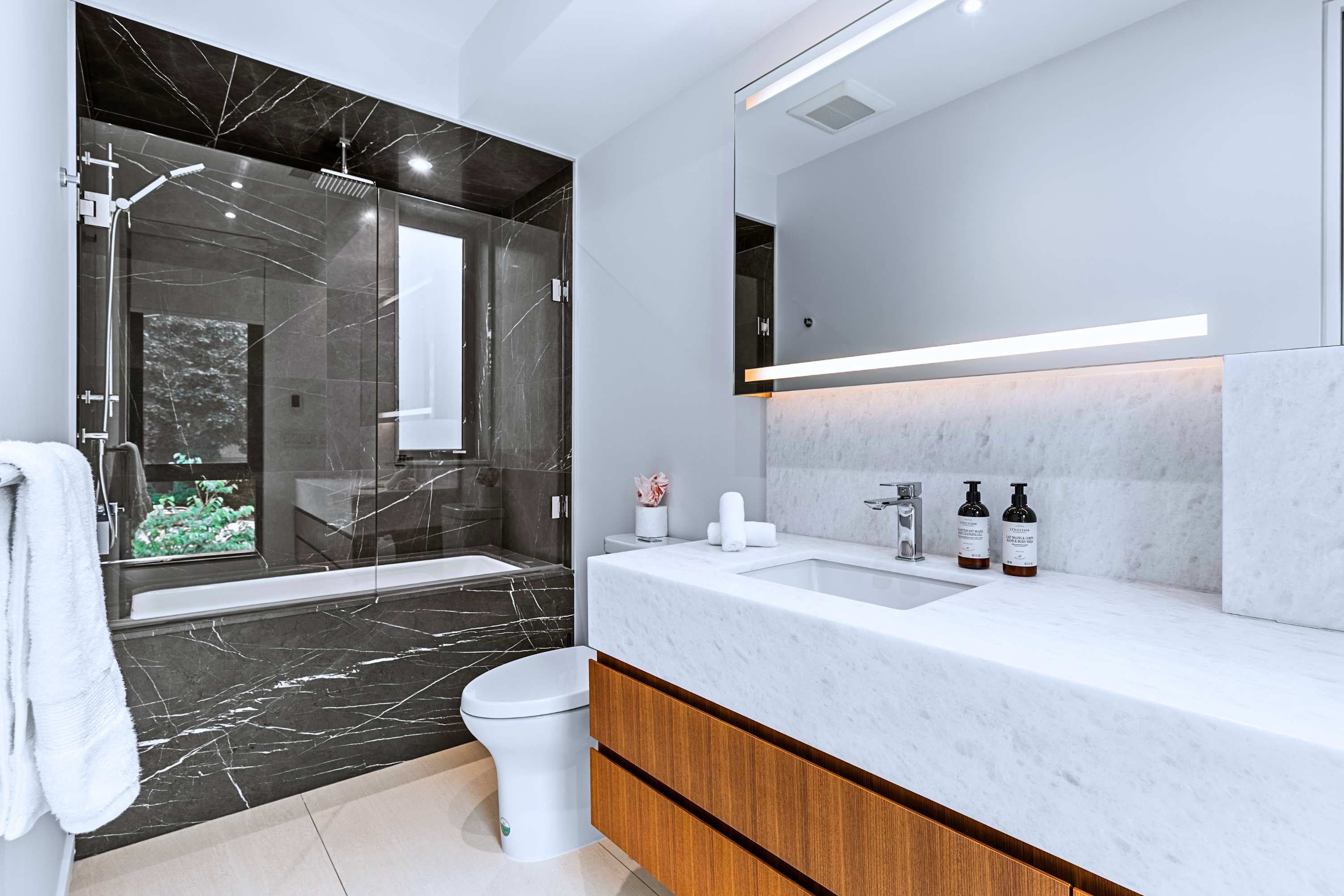 Modern en-suite bath with frameless glass shower and dark marble finishes.