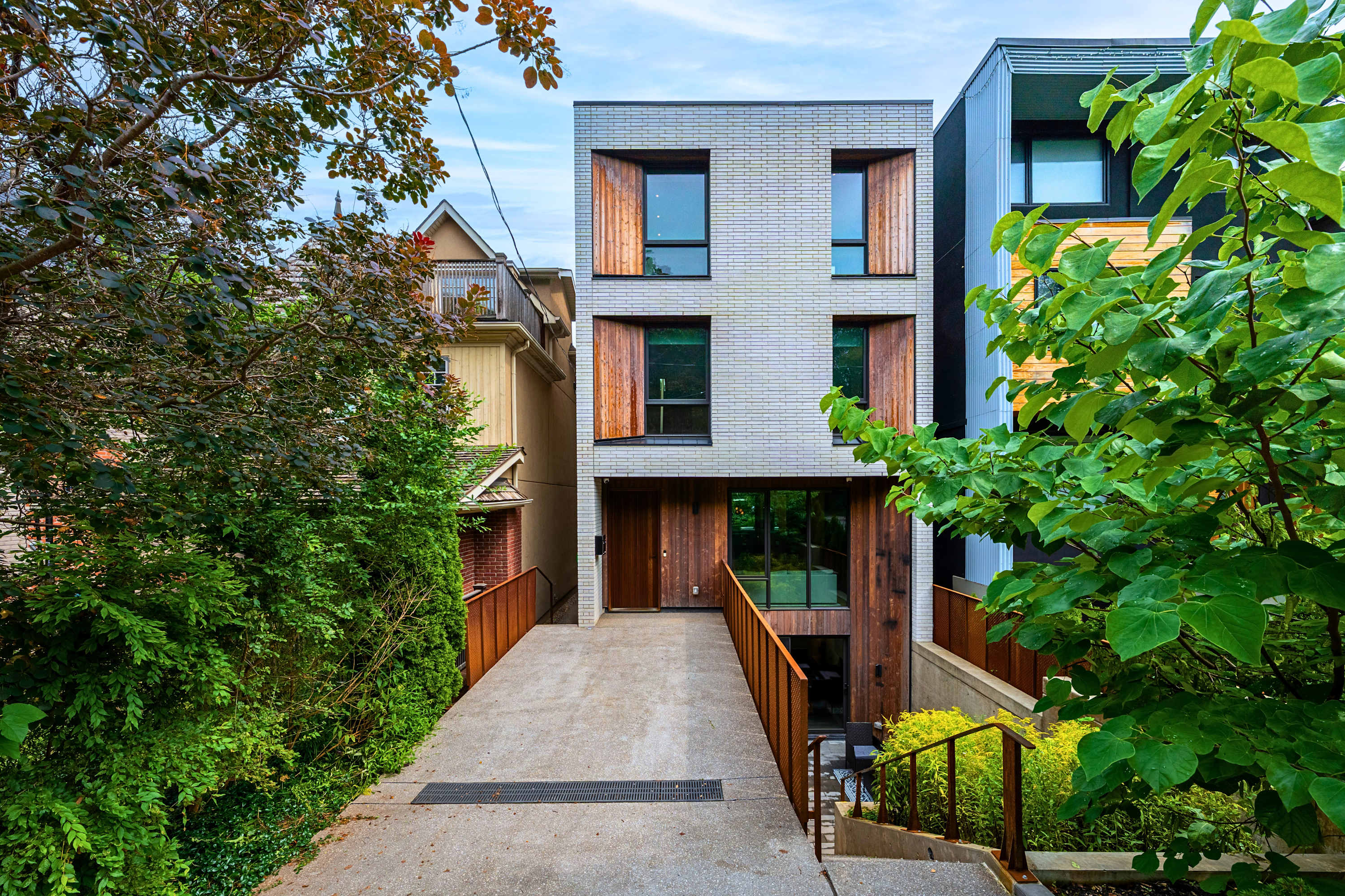 Modern architectural home exterior surrounded by lush trees and a private driveway.