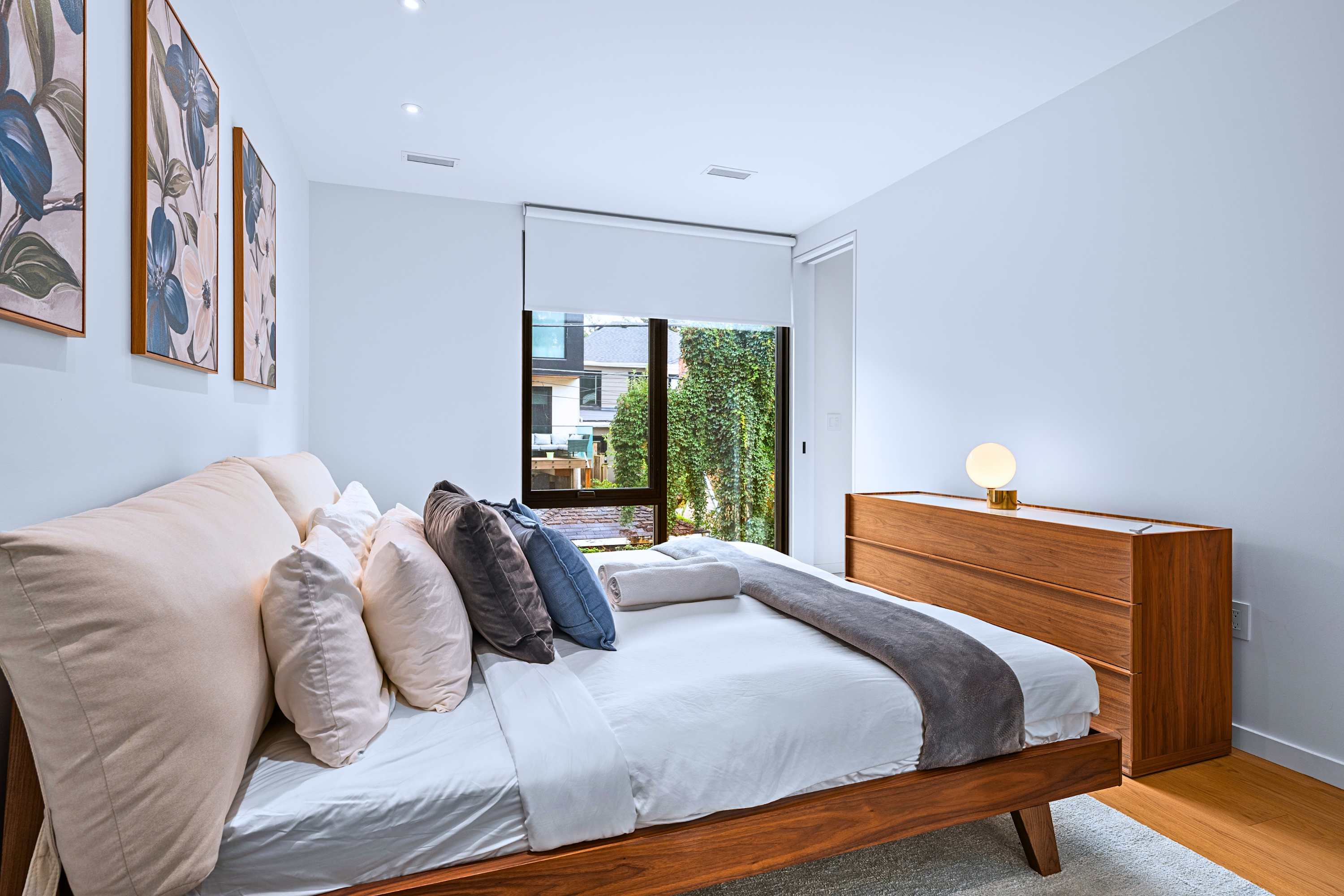 Spacious bedroom featuring bedside lighting, art pieces, and leafy window views.