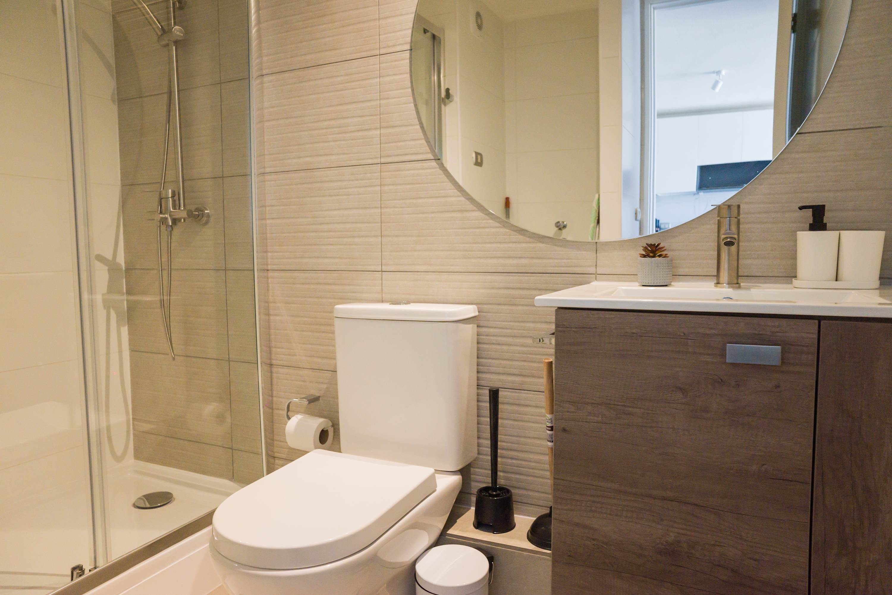 Modern private bathroom with a glass-enclosed shower, textured tile walls, and a wood-look vanity with integrated sink.