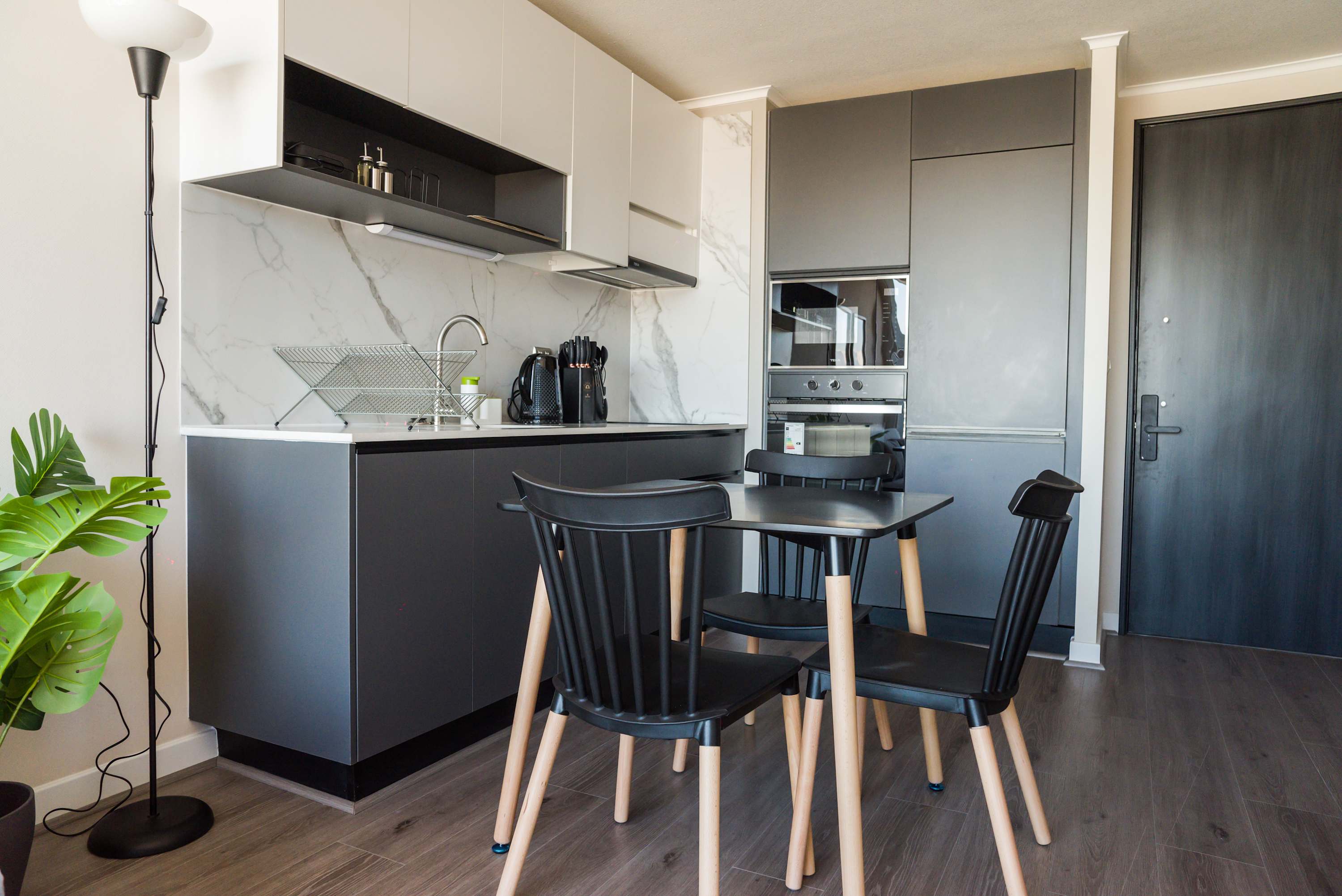 Modern studio kitchen with marble-look backsplash, integrated appliances, and a four-seat dining table for convenient meals at home.