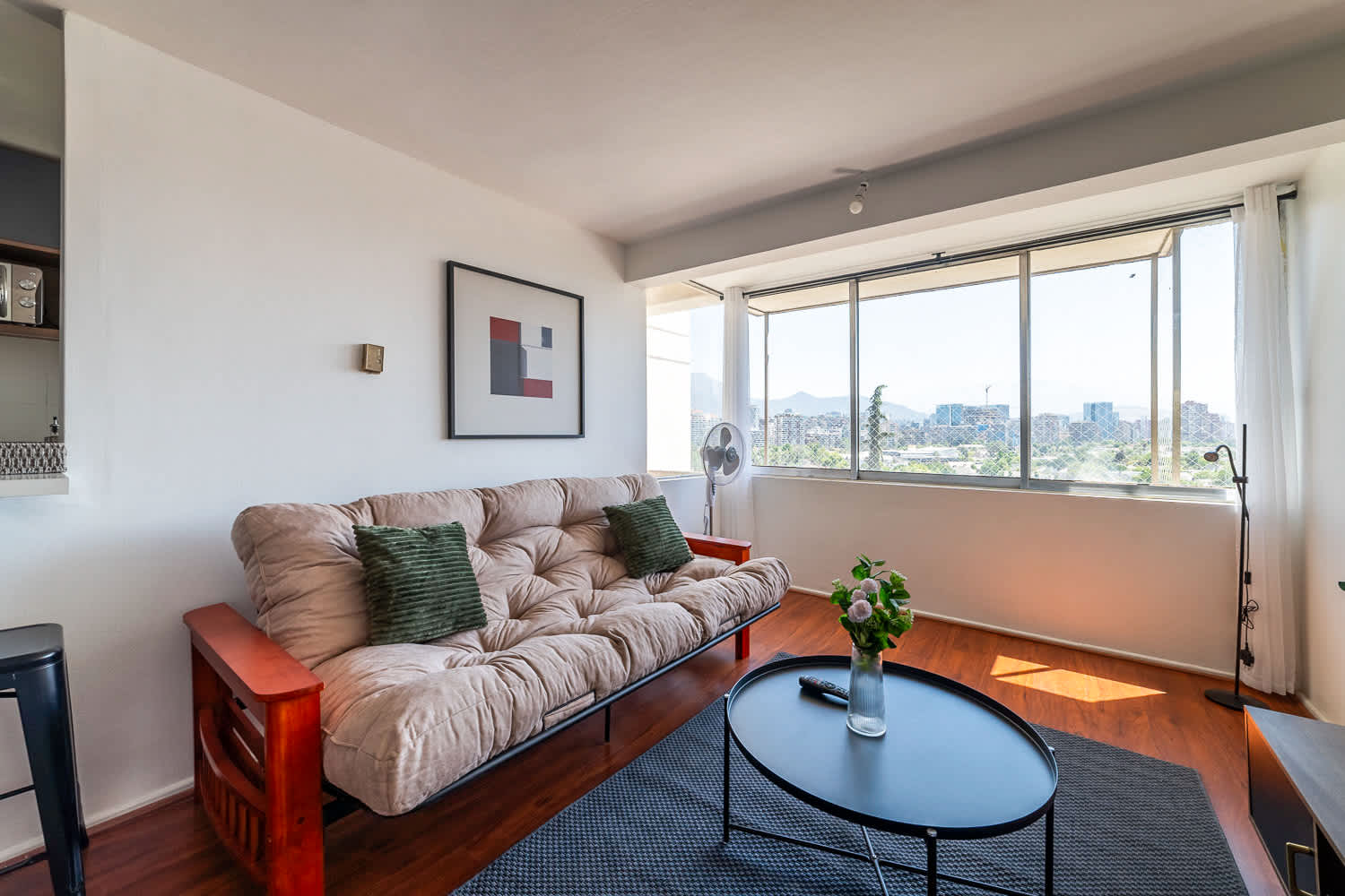 Comfortable living room with a plush sofa, green accent pillows, and expansive windows overlooking Santiago’s cityscape and mountains.