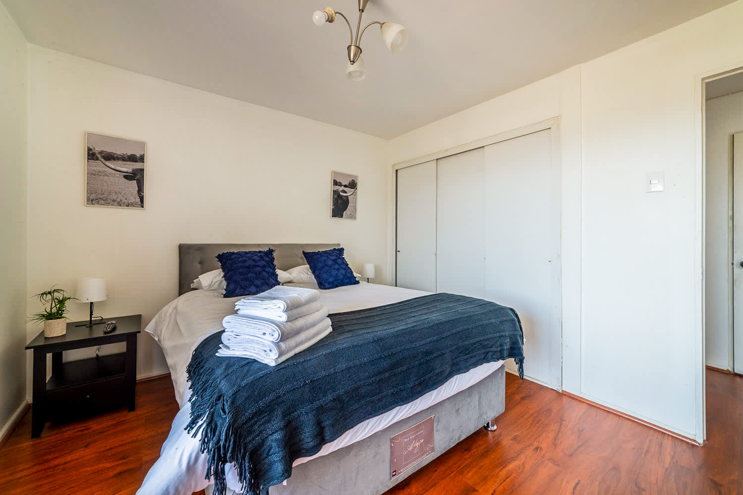 Private bedroom with crisp white bedding, navy textured accents, warm wood flooring, and spacious sliding-door storage.