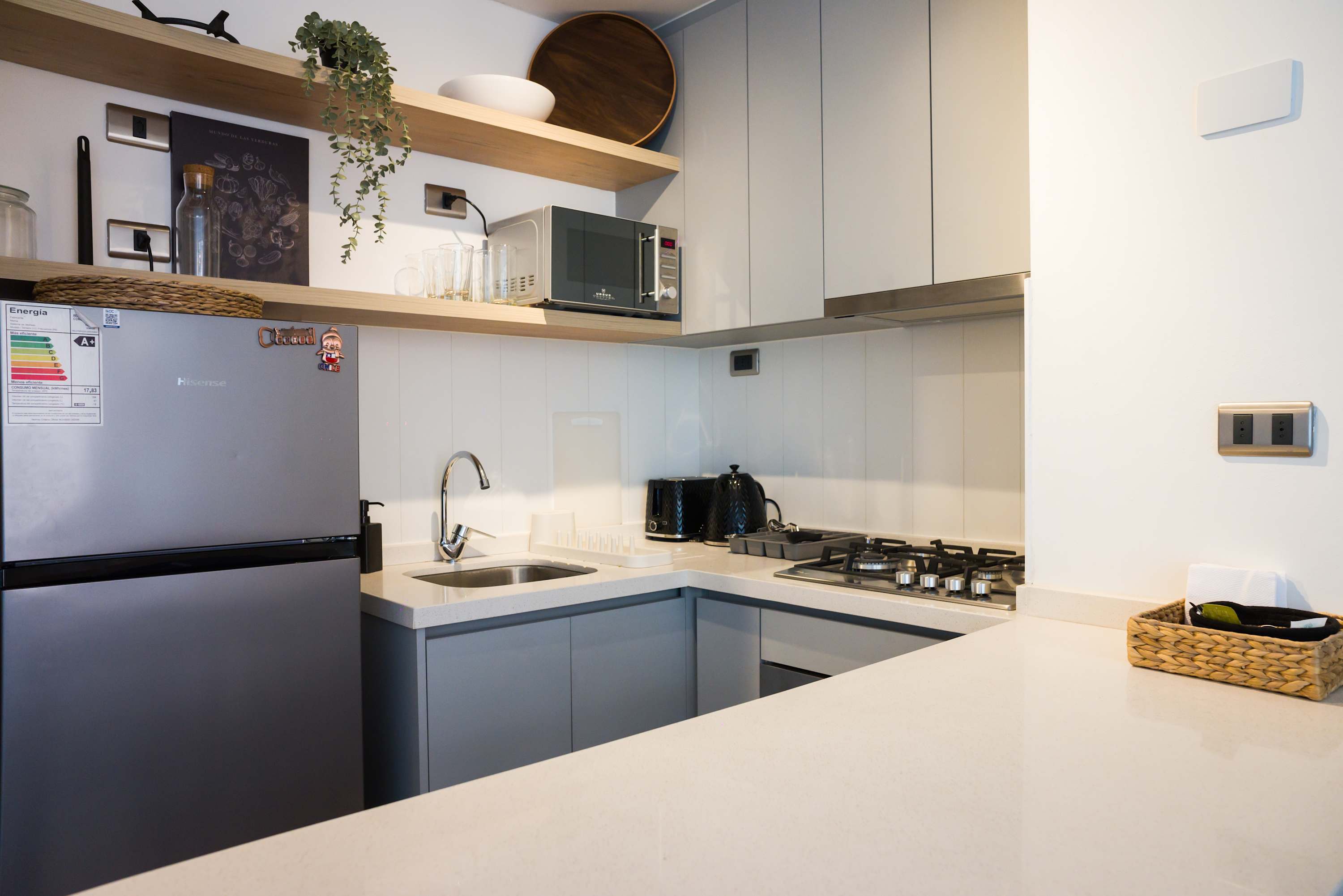 Private kitchen with a four-burner gas cooktop, built-in microwave, full-size refrigerator, and warm wood shelving with glassware and greenery.