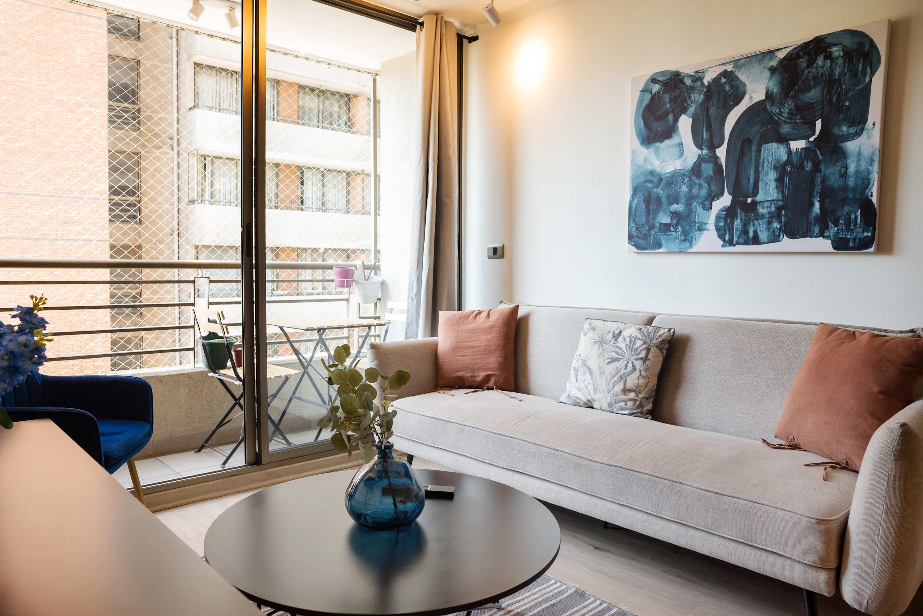 Bright living room with a spacious sectional, blue glass accents, and a balcony dining nook overlooking the city.