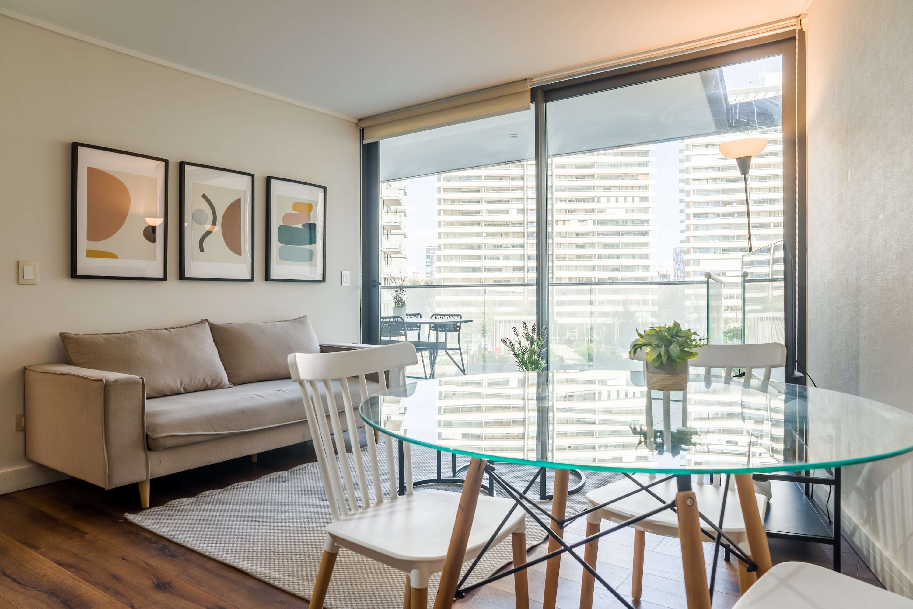 Bright living and dining area with a glass table, comfortable sofa, and floor-to-ceiling windows overlooking Santiago’s high-rise cityscape.