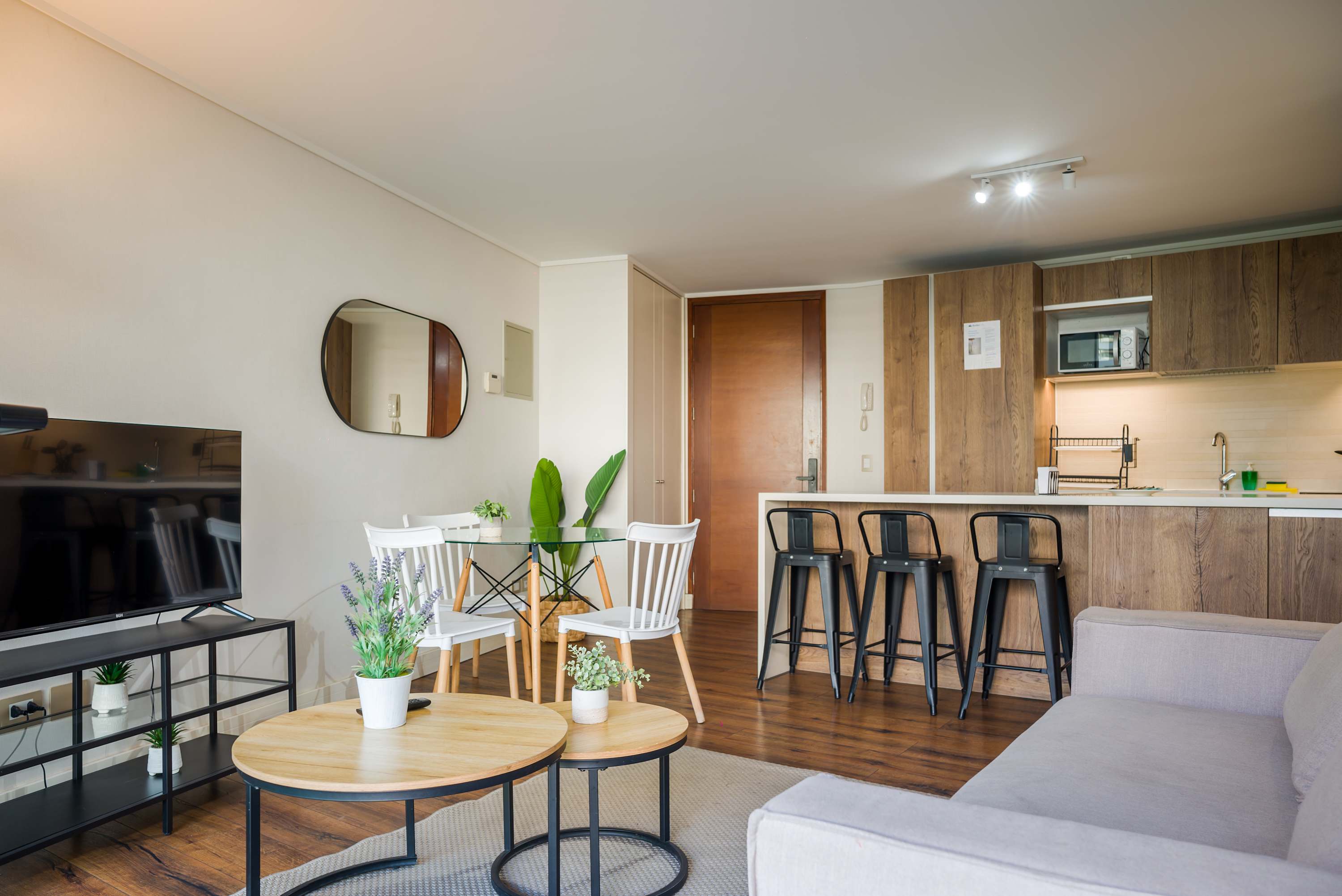 Open-plan living area with a light gray sofa, round wood coffee tables, and a modern kitchen island with bar seating.