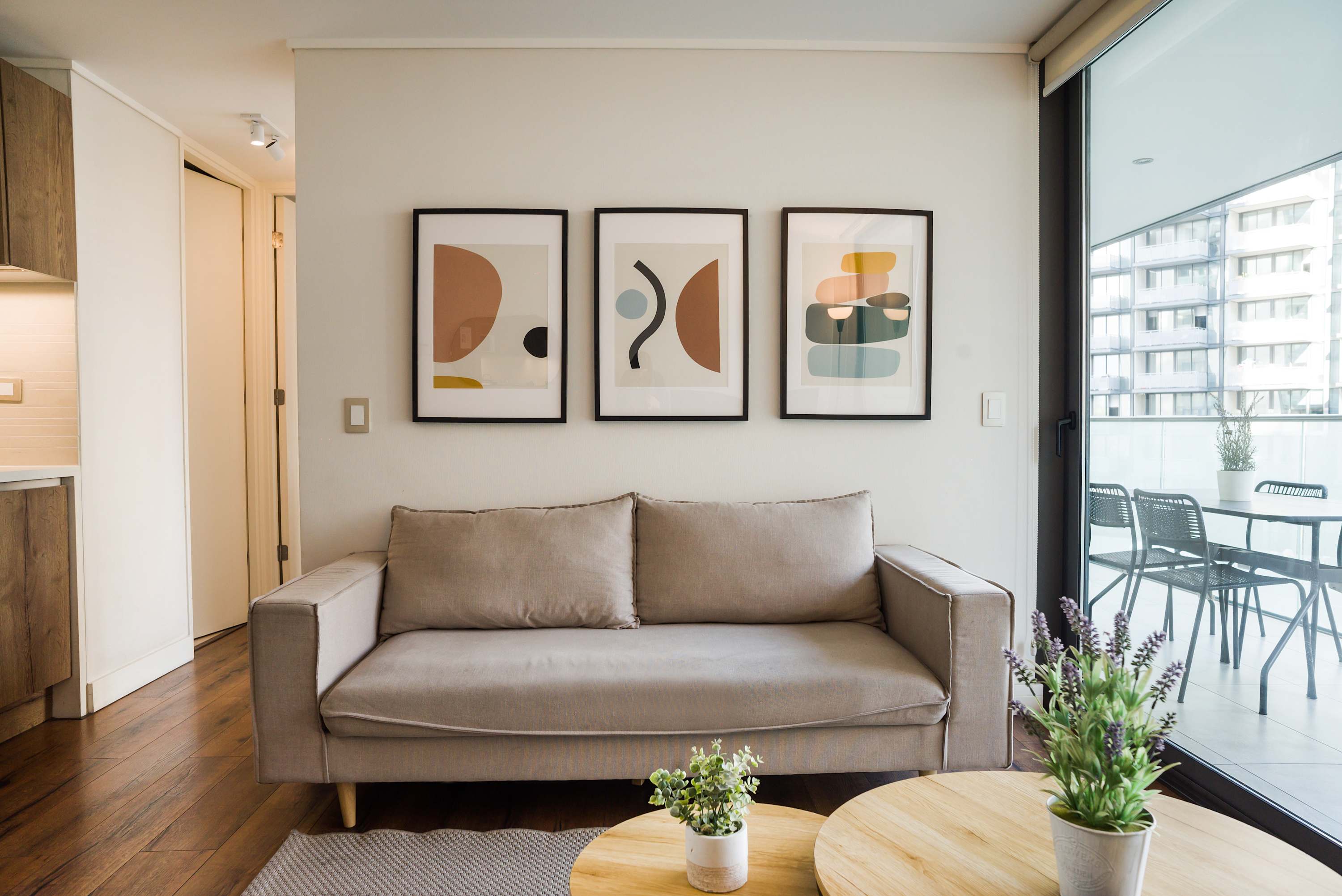 Private living room with a comfortable beige sofa, colorful abstract artwork, and floor-to-ceiling windows opening to a furnished balcony.