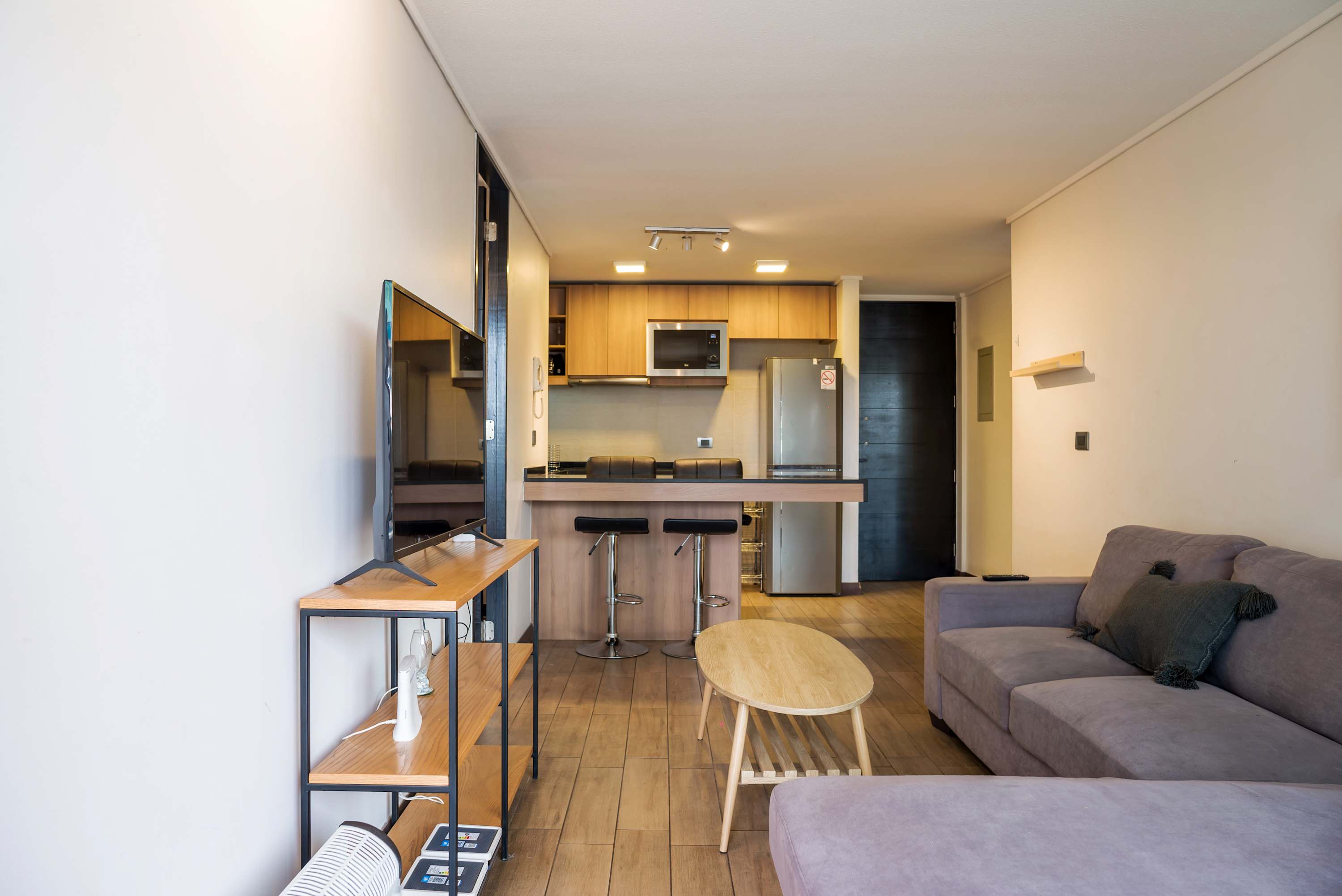 Open-plan living room with a comfortable sectional, oval wood coffee table, and breakfast bar beside the fully equipped kitchen.