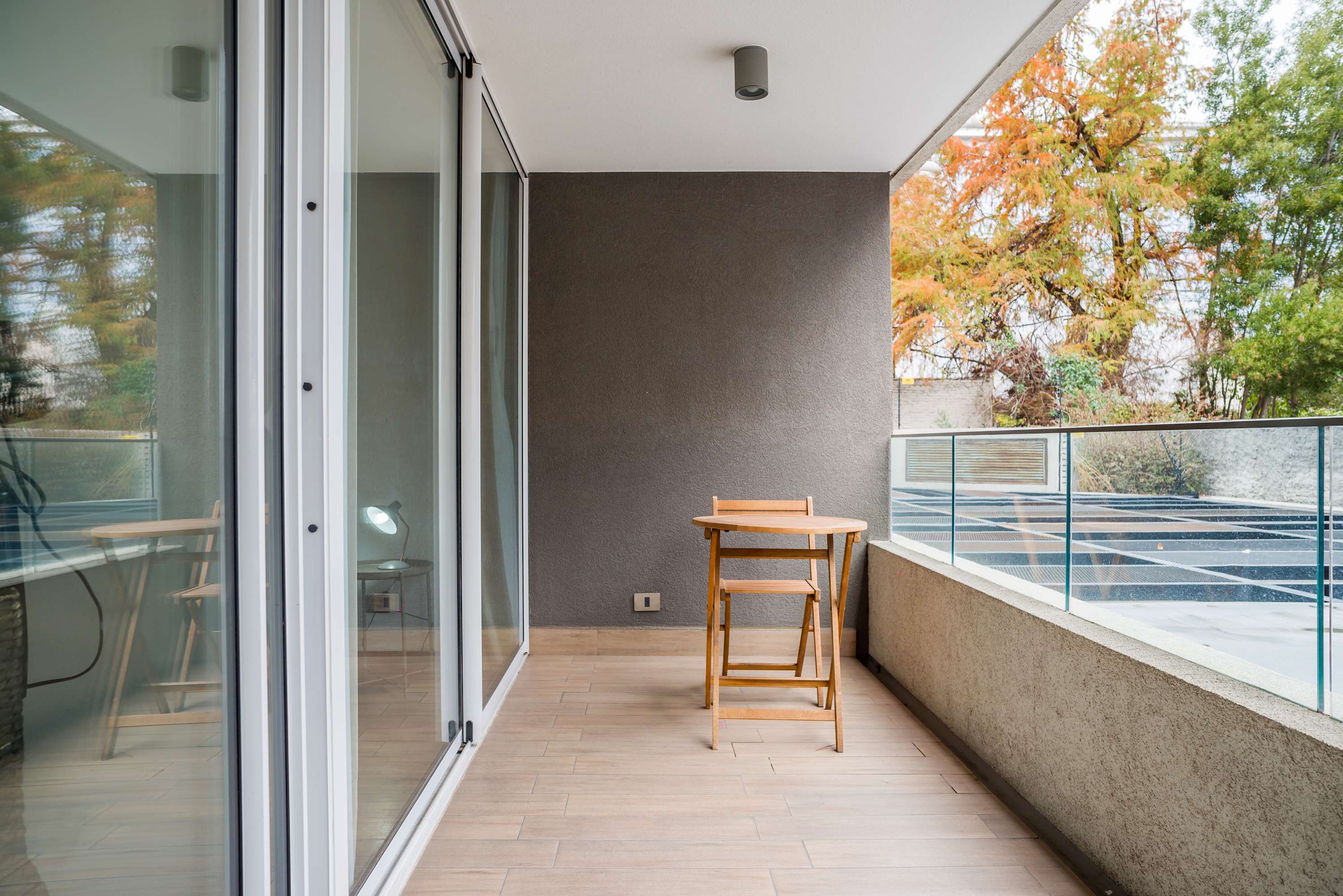 Private balcony with a wooden café table, glass railing, and leafy seasonal views.