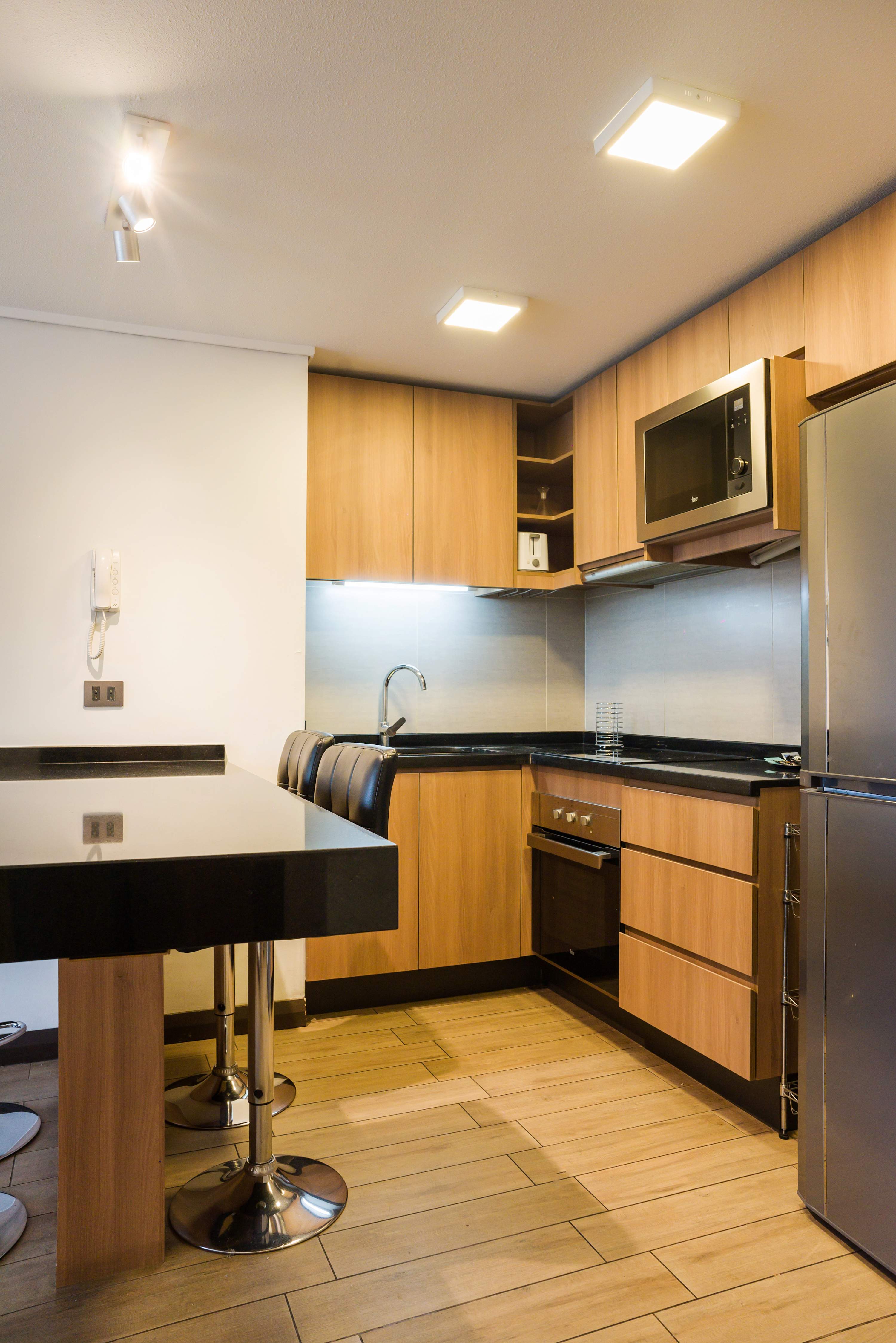 Fully equipped kitchen with warm wood cabinetry, black granite counters, stainless-steel appliances, and a two-seat breakfast peninsula.