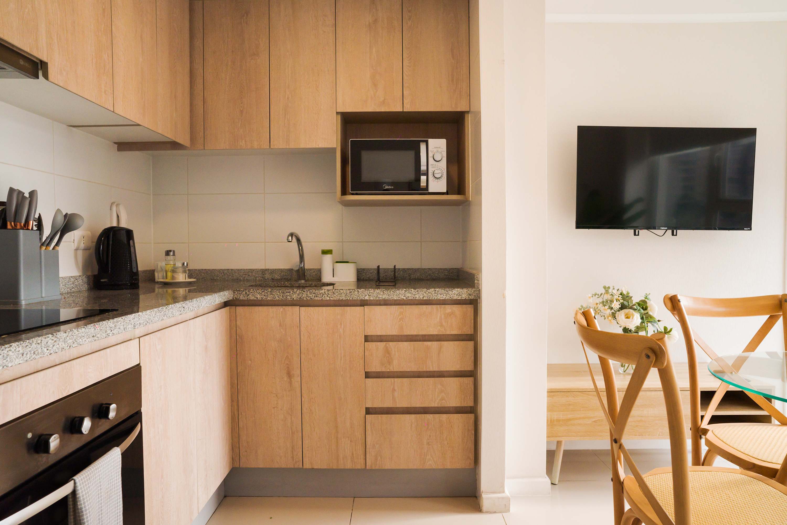 Well-equipped apartment kitchen with warm wood cabinetry, granite counters, and a dining nook with a glass table and wooden chairs.