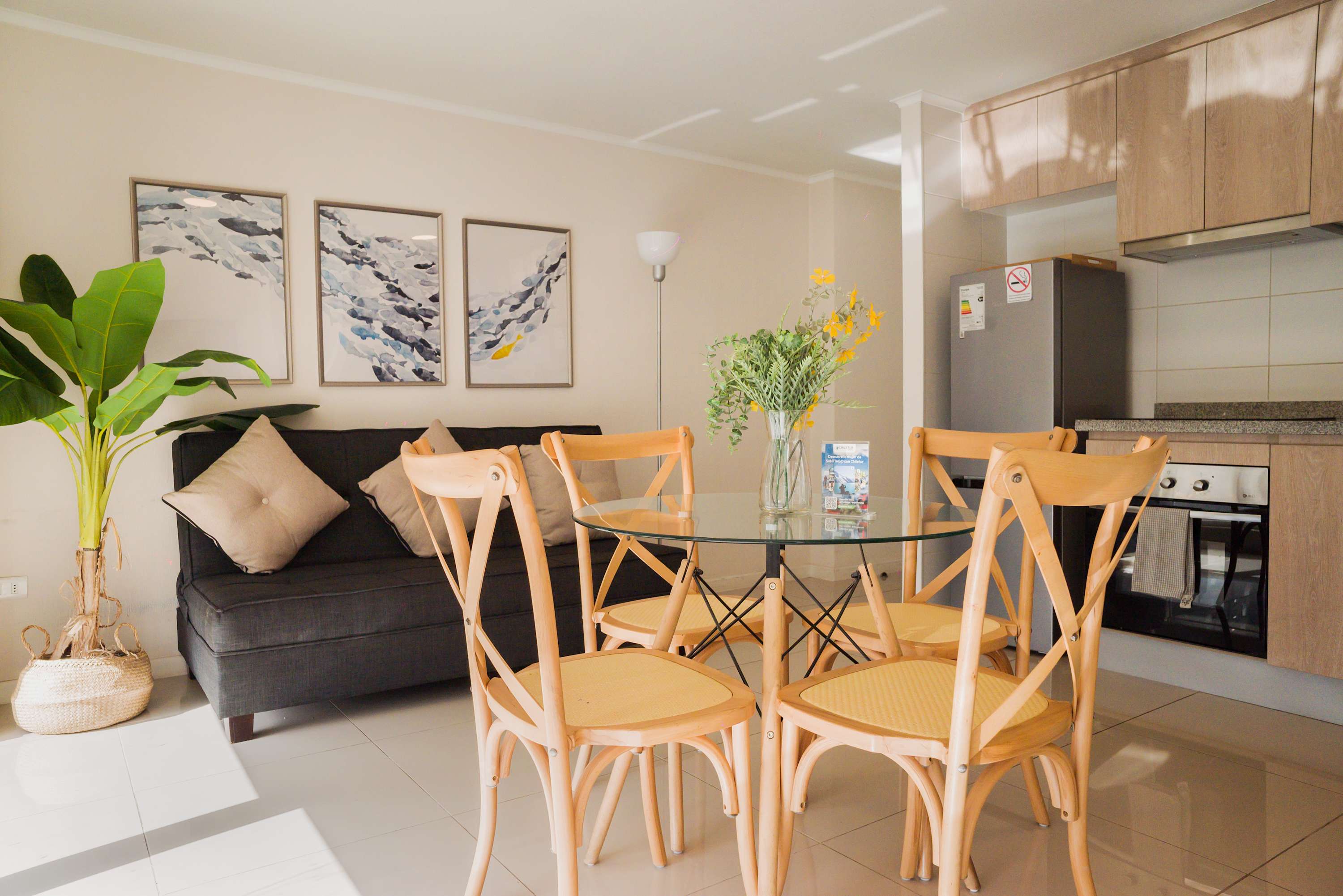 Open-plan studio living area with a comfortable sofa, glass dining table, and fully equipped wood-finish kitchen.