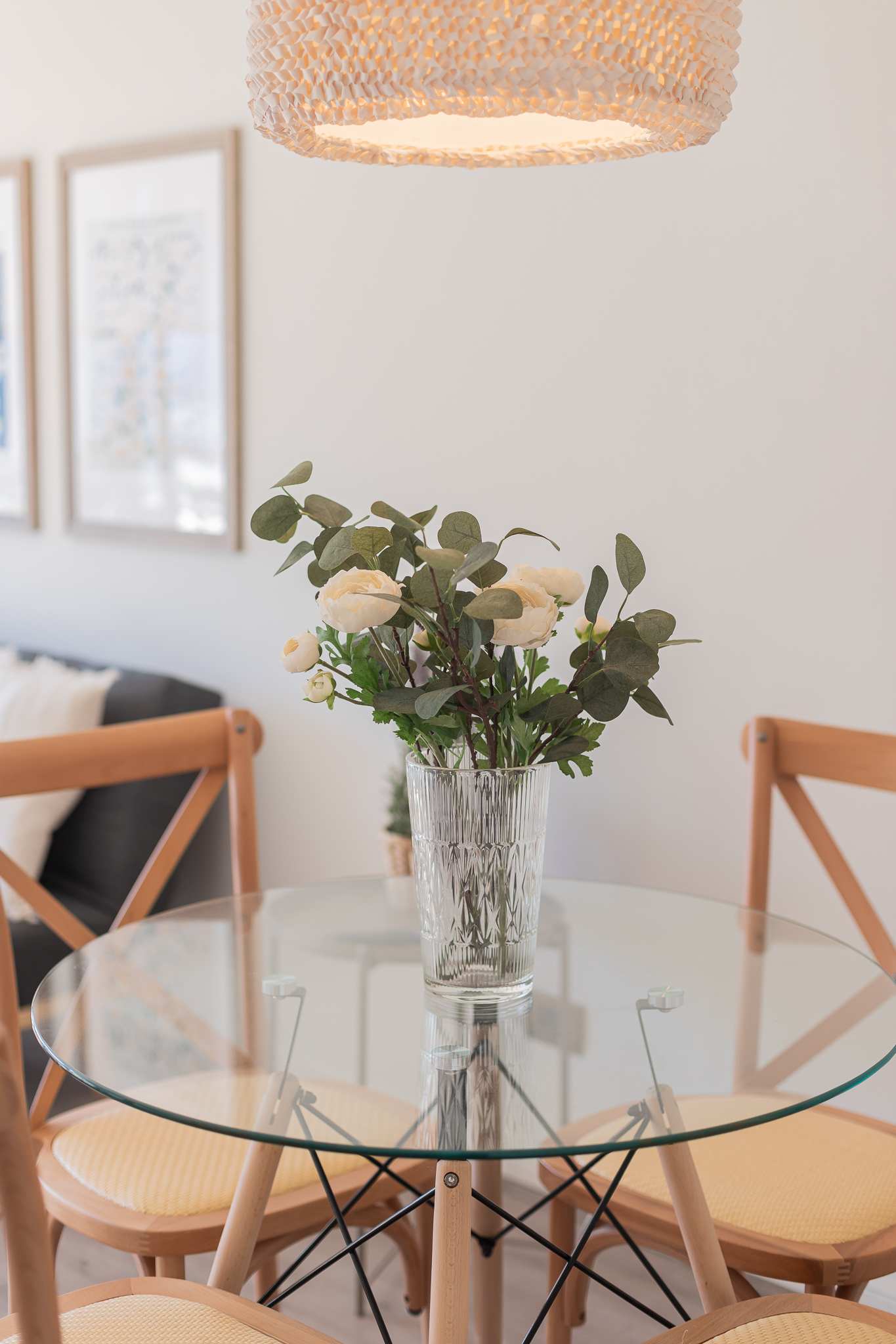 Private dining nook with a round glass table, sculptural woven pendant light, and fresh floral centerpiece.