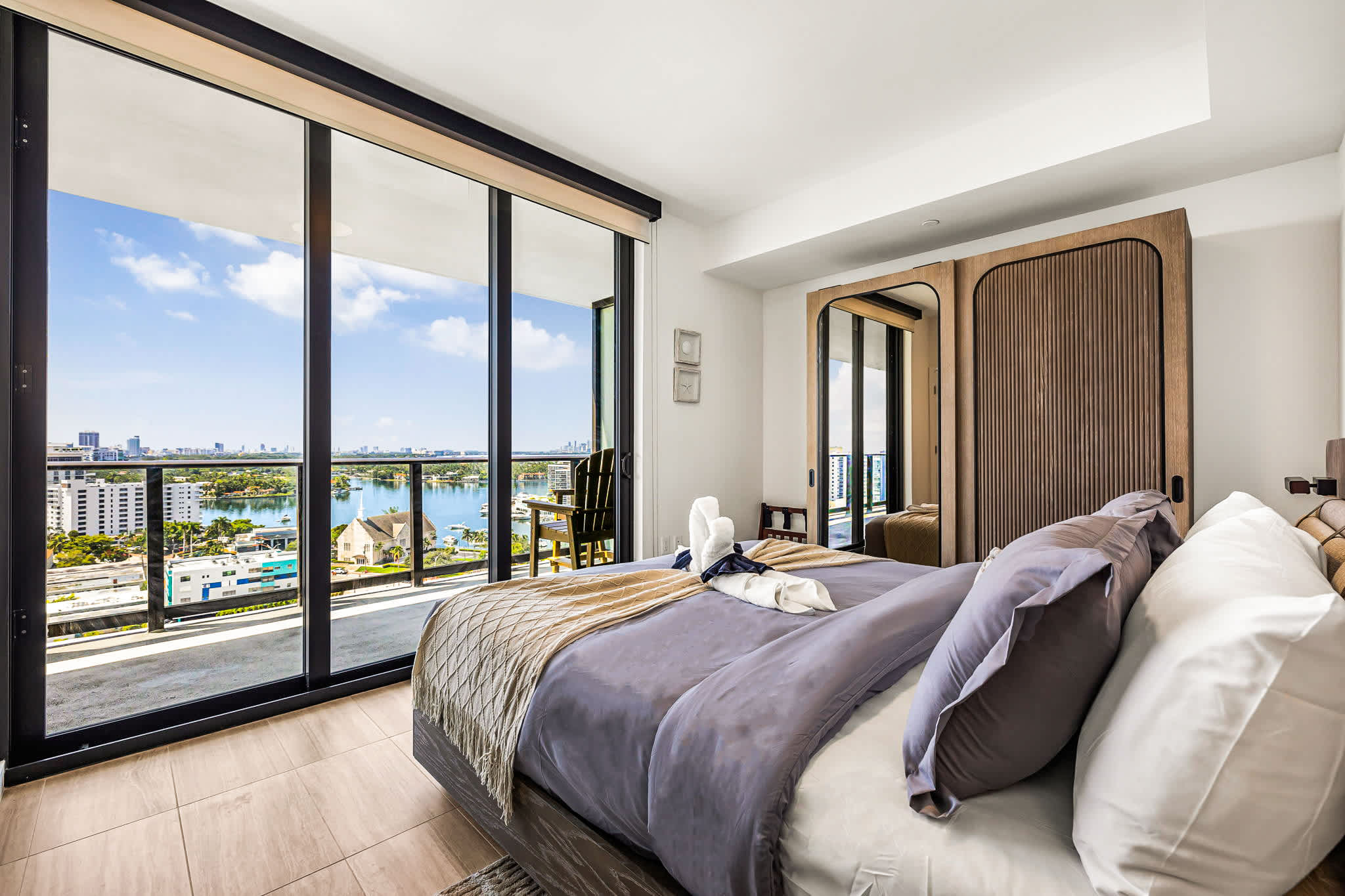Private bedroom with floor-to-ceiling glass doors overlooking the marina, city skyline, and sparkling waterfront.