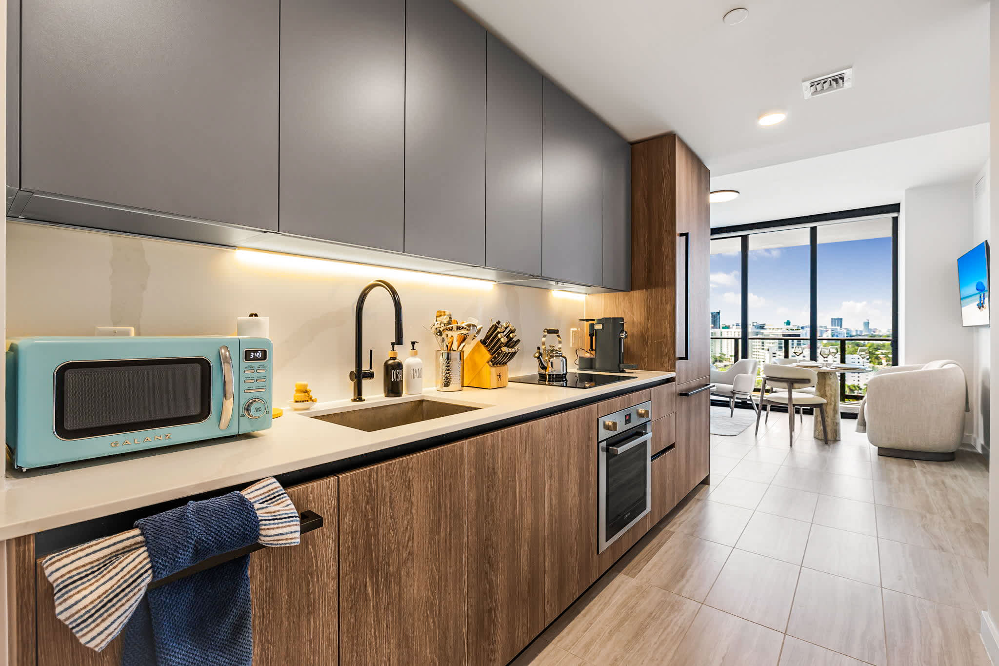 Modern open kitchen with a turquoise retro microwave, full-size appliances, and bright city views through floor-to-ceiling windows.