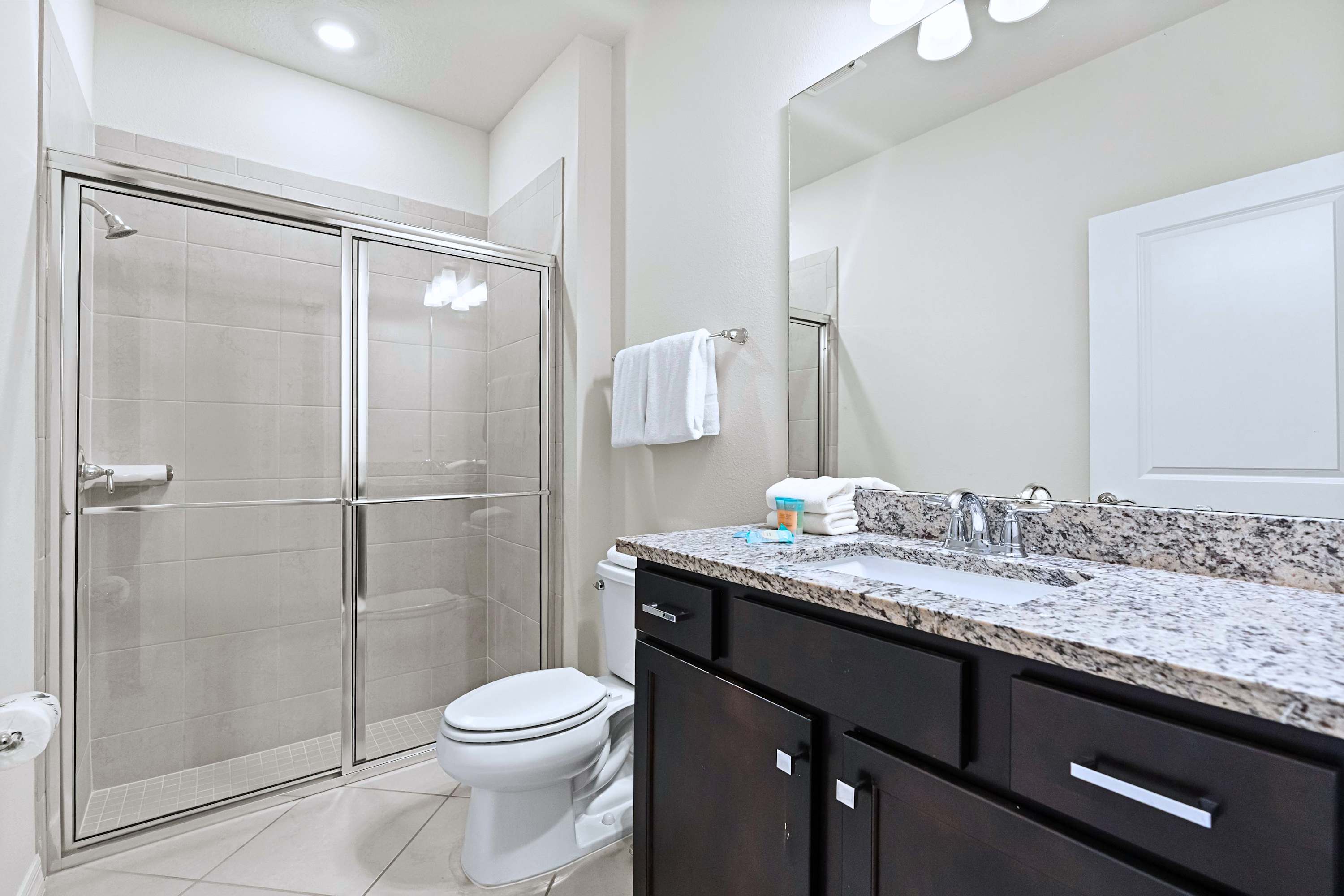 A spotless, highly functional bathroom with a step-in shower and bright vanity lighting.
