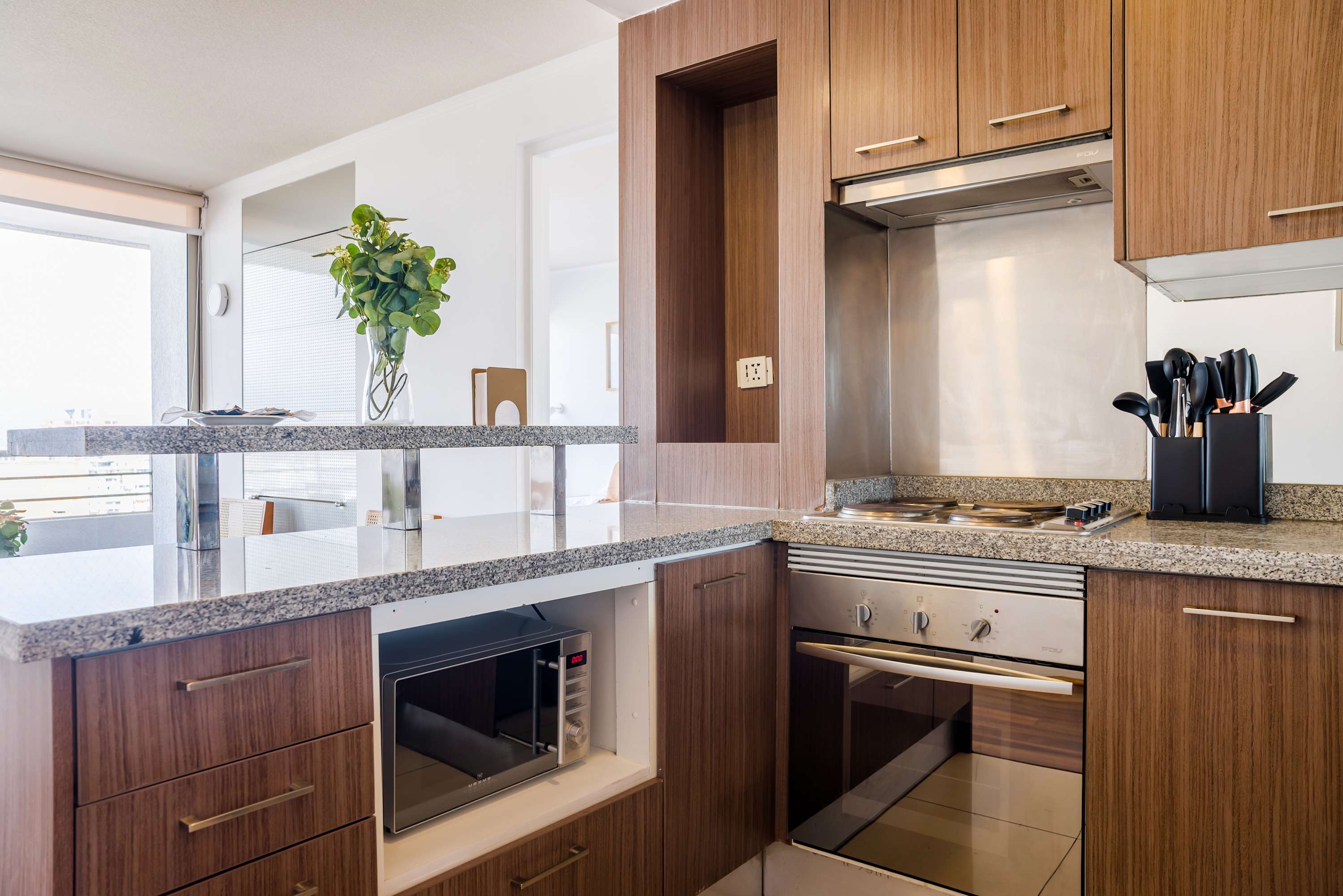 Private kitchen with warm wood cabinetry, granite counters, full-size cooking appliances, and a bright dining peninsula beside the window.