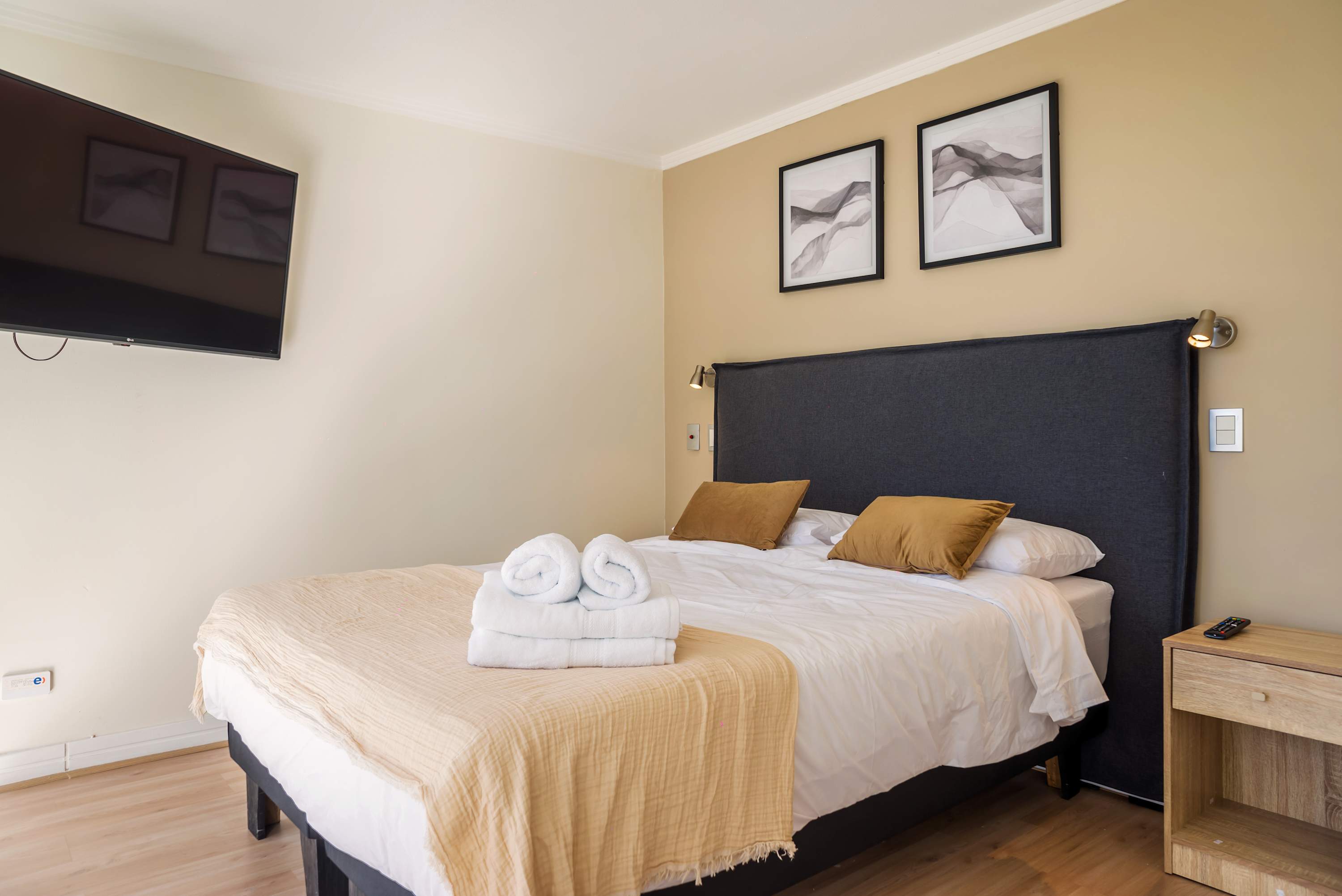 Private bedroom with a charcoal upholstered headboard, crisp white bedding, cozy beige throw, and wall-mounted TV.