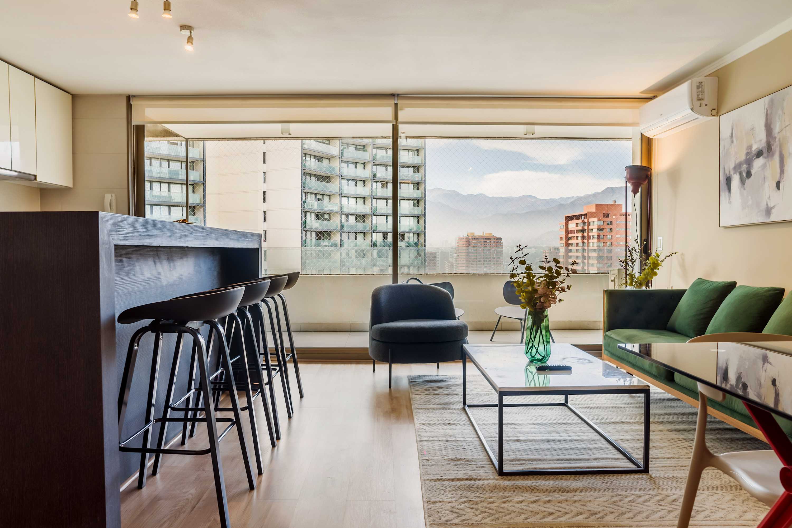 Contemporary living room with a green sofa, breakfast bar seating, and sweeping mountain views through floor-to-ceiling windows.