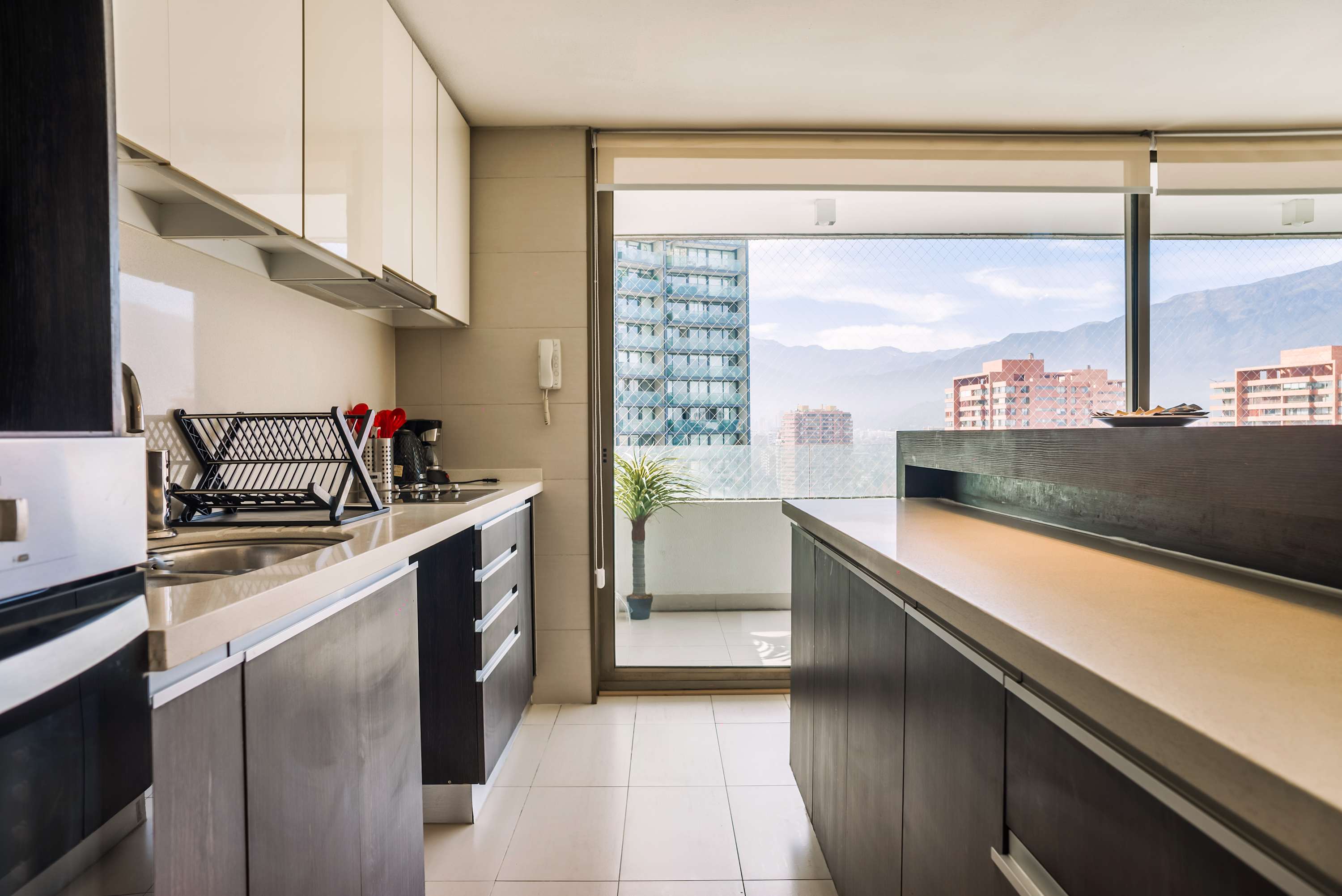 Modern galley kitchen with generous counter space, opening to a bright balcony and panoramic mountain-and-city views.