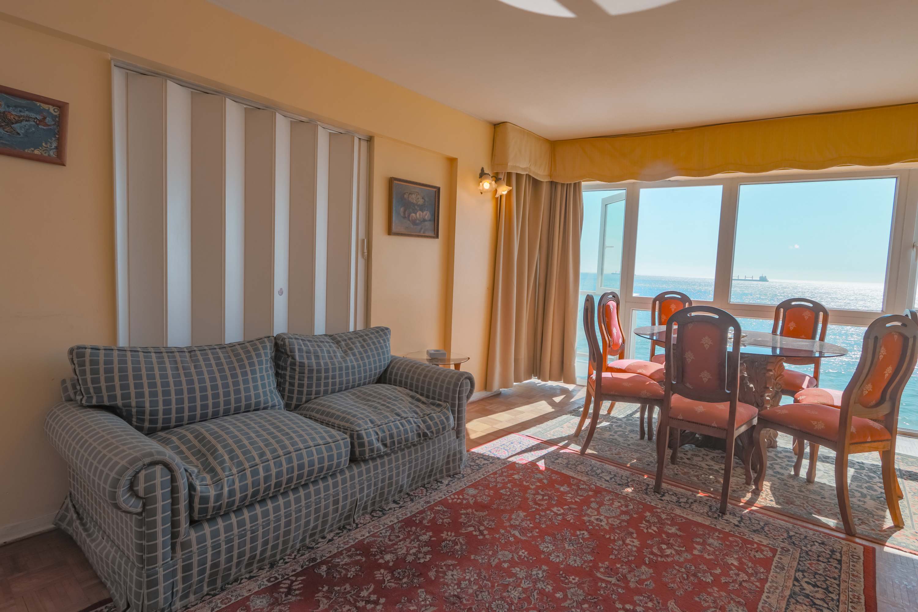 Cozy living and dining area with a classic checkered sofa, elegant seating, and sweeping ocean views through expansive windows.