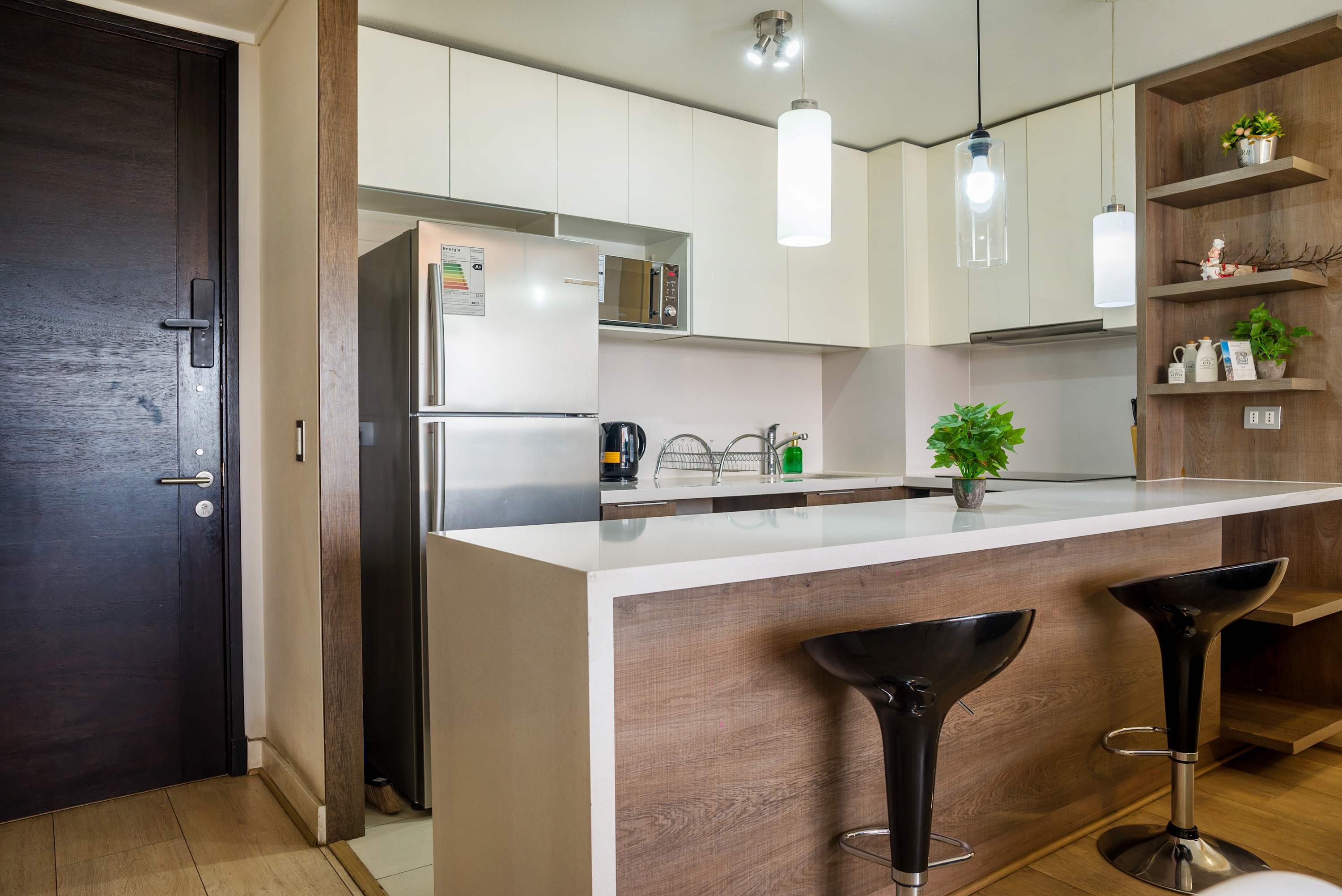 Modern kitchen with a quartz breakfast bar, two bar stools, stainless-steel appliances, and warm wood cabinetry.