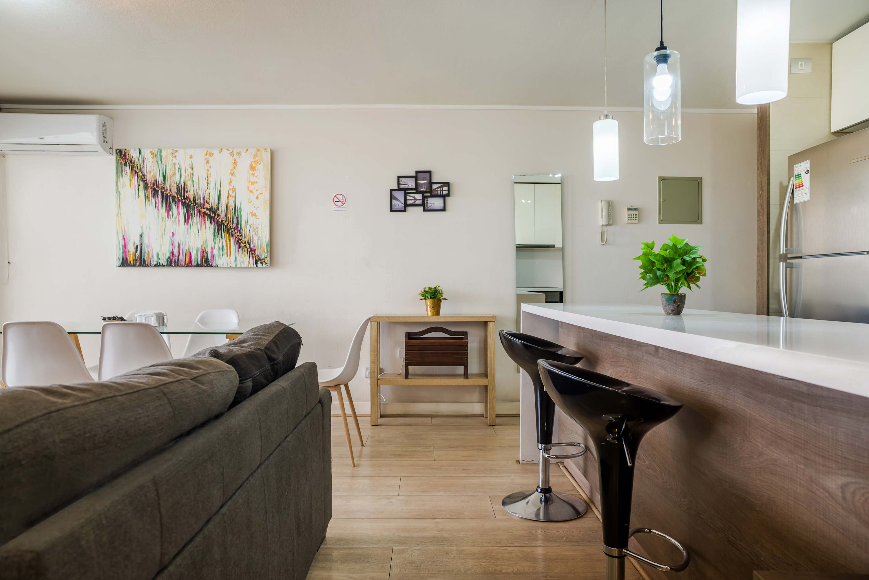 Open-plan living and dining area with a colorful abstract artwork, comfortable sofa, and sleek kitchen island with bar seating.