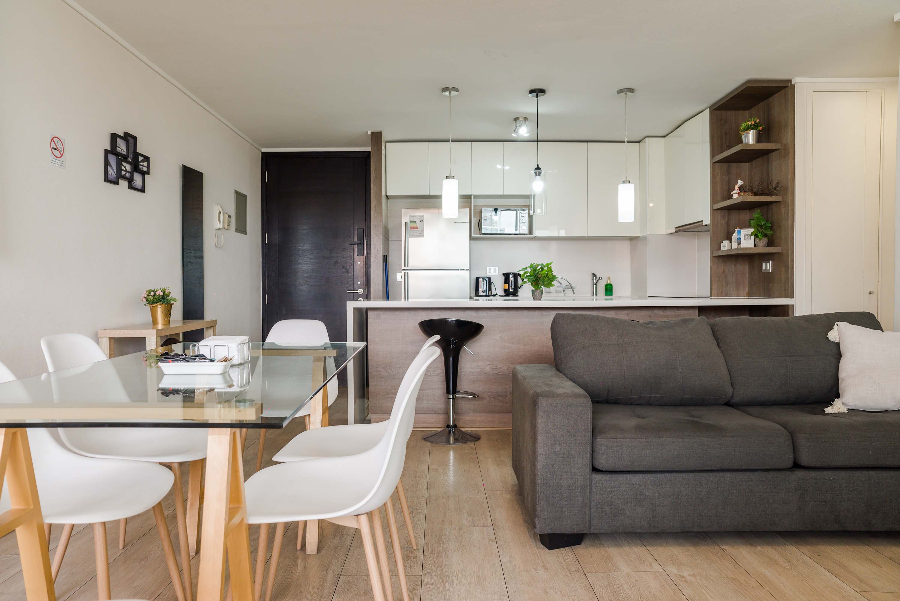 Open-plan living area with a comfortable gray sectional, dining table, and sleek white kitchen with modern pendant lighting.