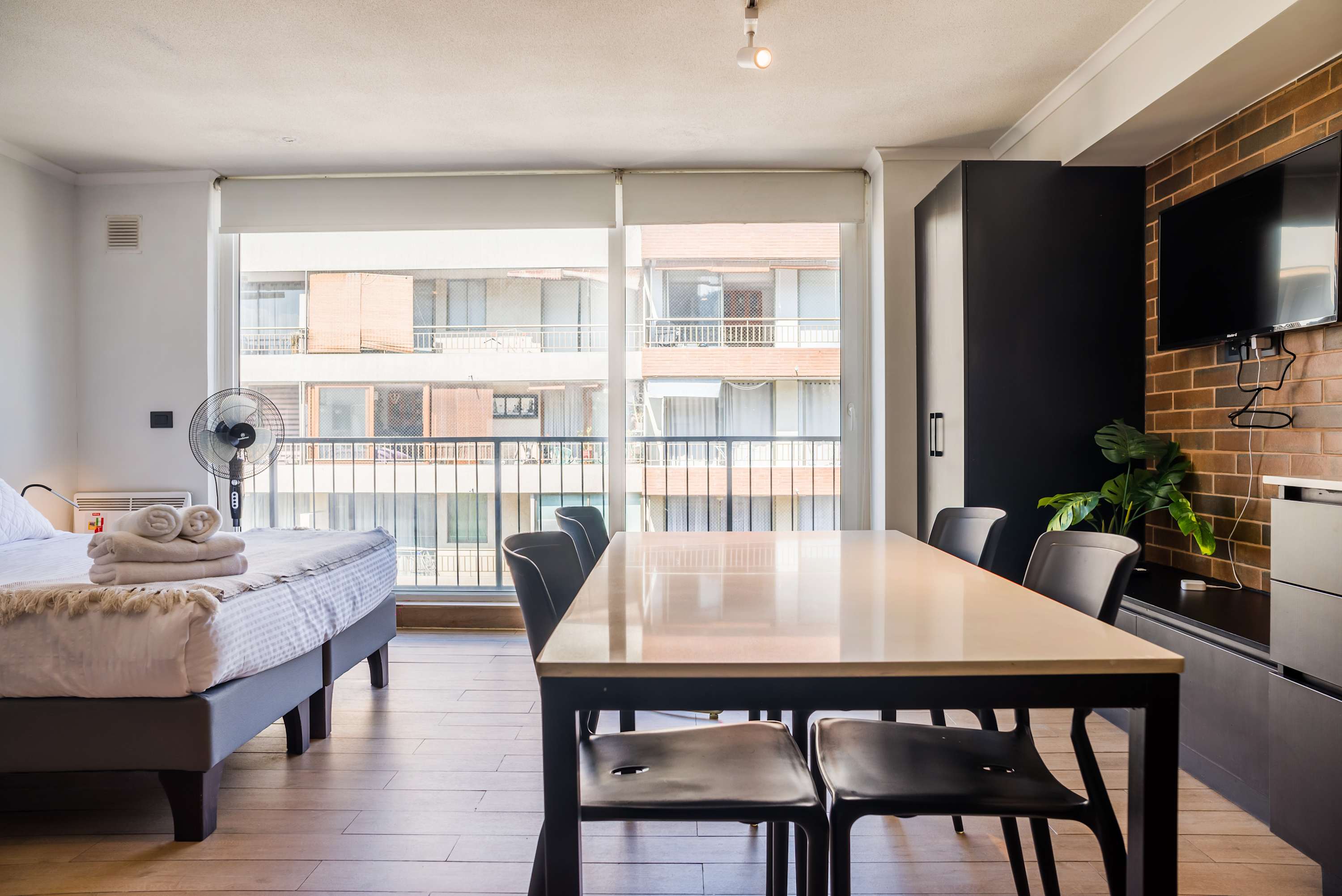 Open-plan dining area with a generous table, black seating, and floor-to-ceiling windows overlooking the surrounding neighborhood.