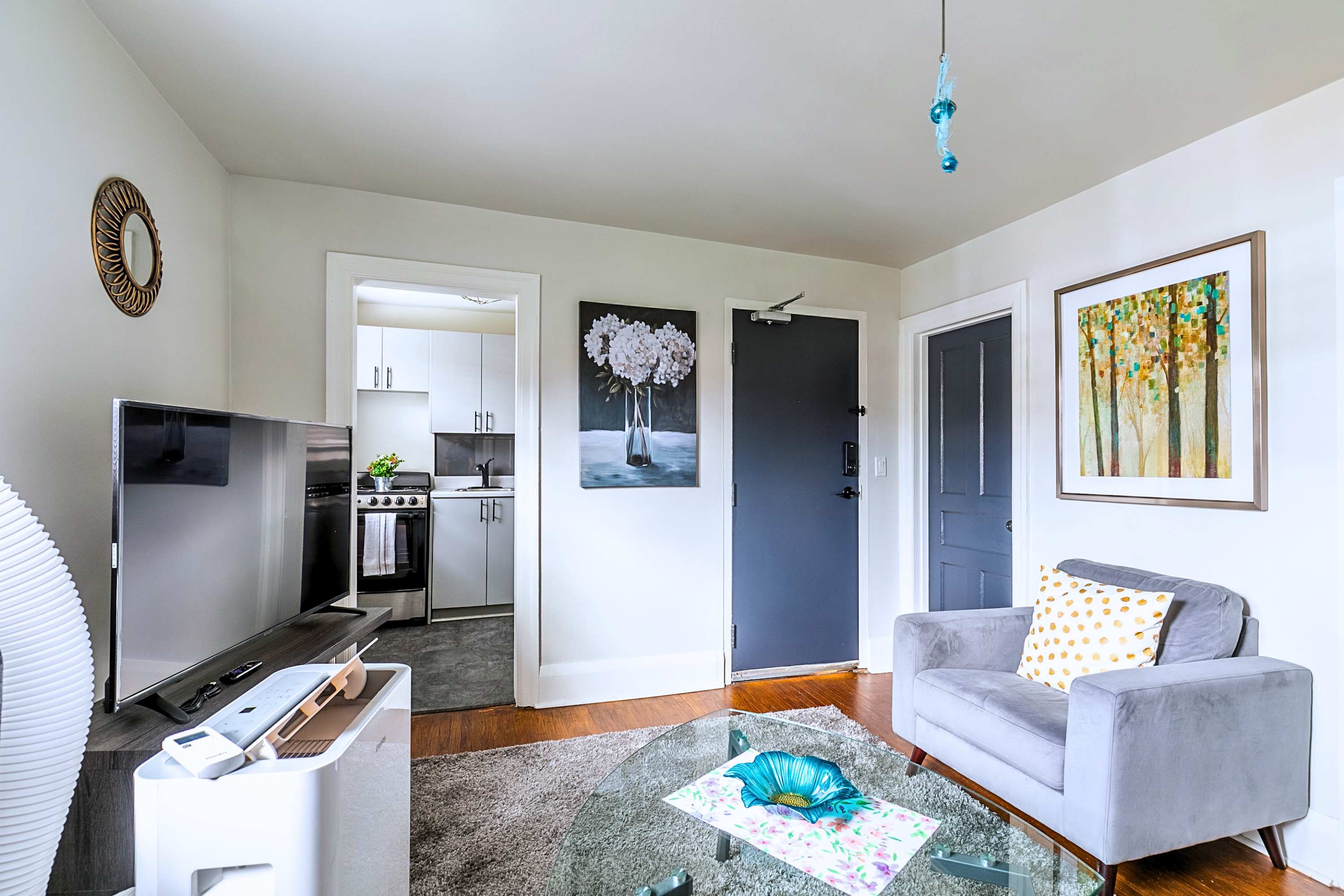 Cozy seating area featuring a plush armchair, flat-screen TV, and view into the kitchen