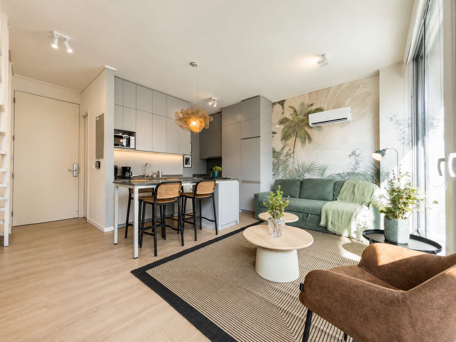 Open-plan living room with a green sofa, botanical mural, and bright floor-to-ceiling windows