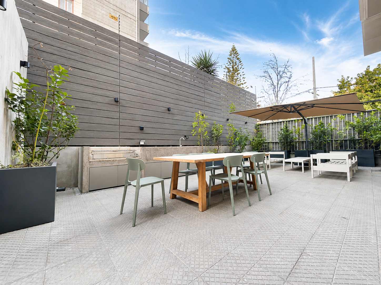 Sunny outdoor dining terrace with a built-in sink, generous seating, leafy planters, and a shade umbrella for relaxed al fresco meals.
