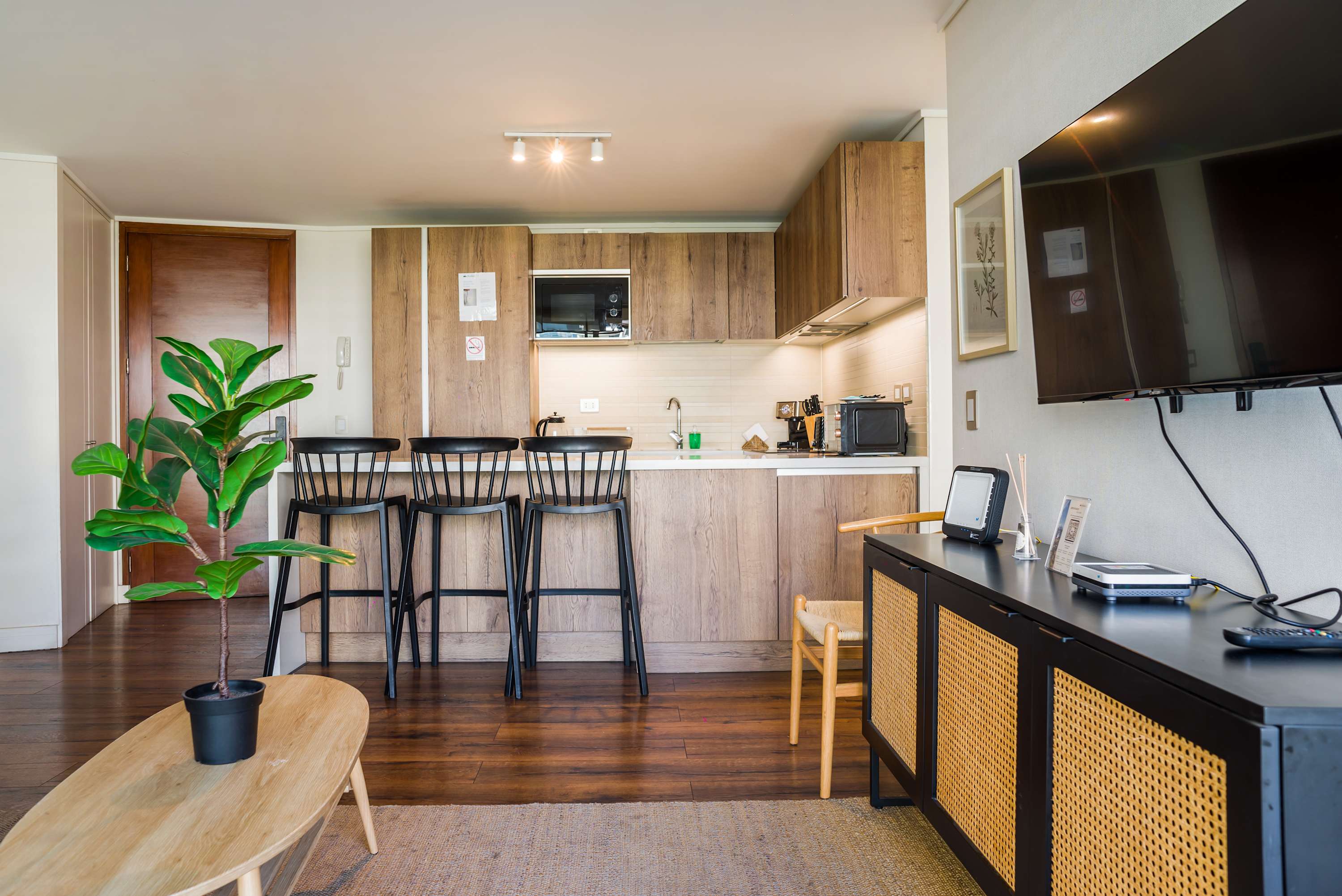 Open-plan living room with a sleek wood kitchen, three-seat breakfast bar, and warm natural finishes.