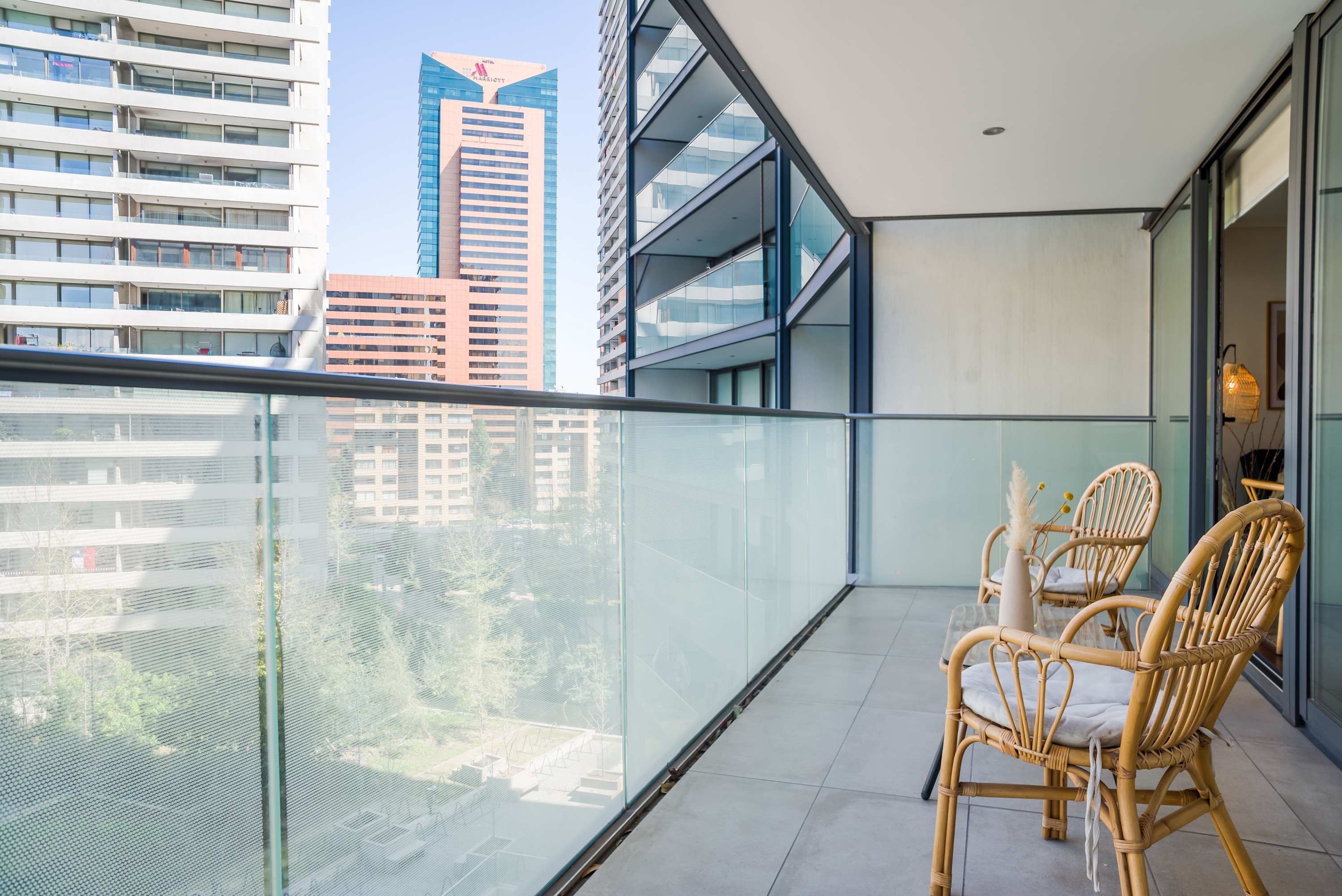 Private balcony with rattan seating, clear glass railings, and sweeping views of Santiago’s modern high-rise skyline.