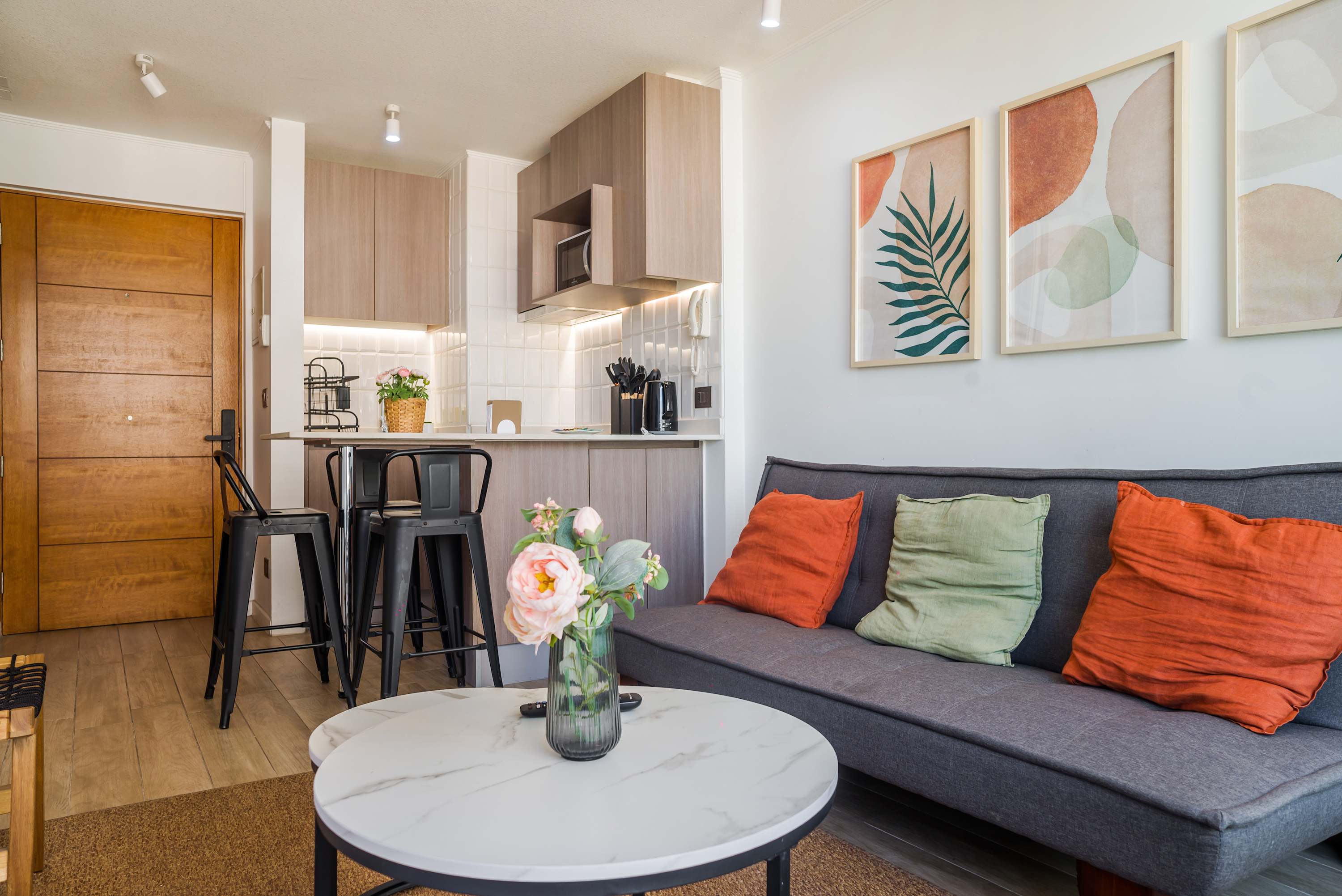 Private studio living area with a comfortable gray sectional, colorful cushions, marble-look coffee table, and a fully equipped open kitchenette.
