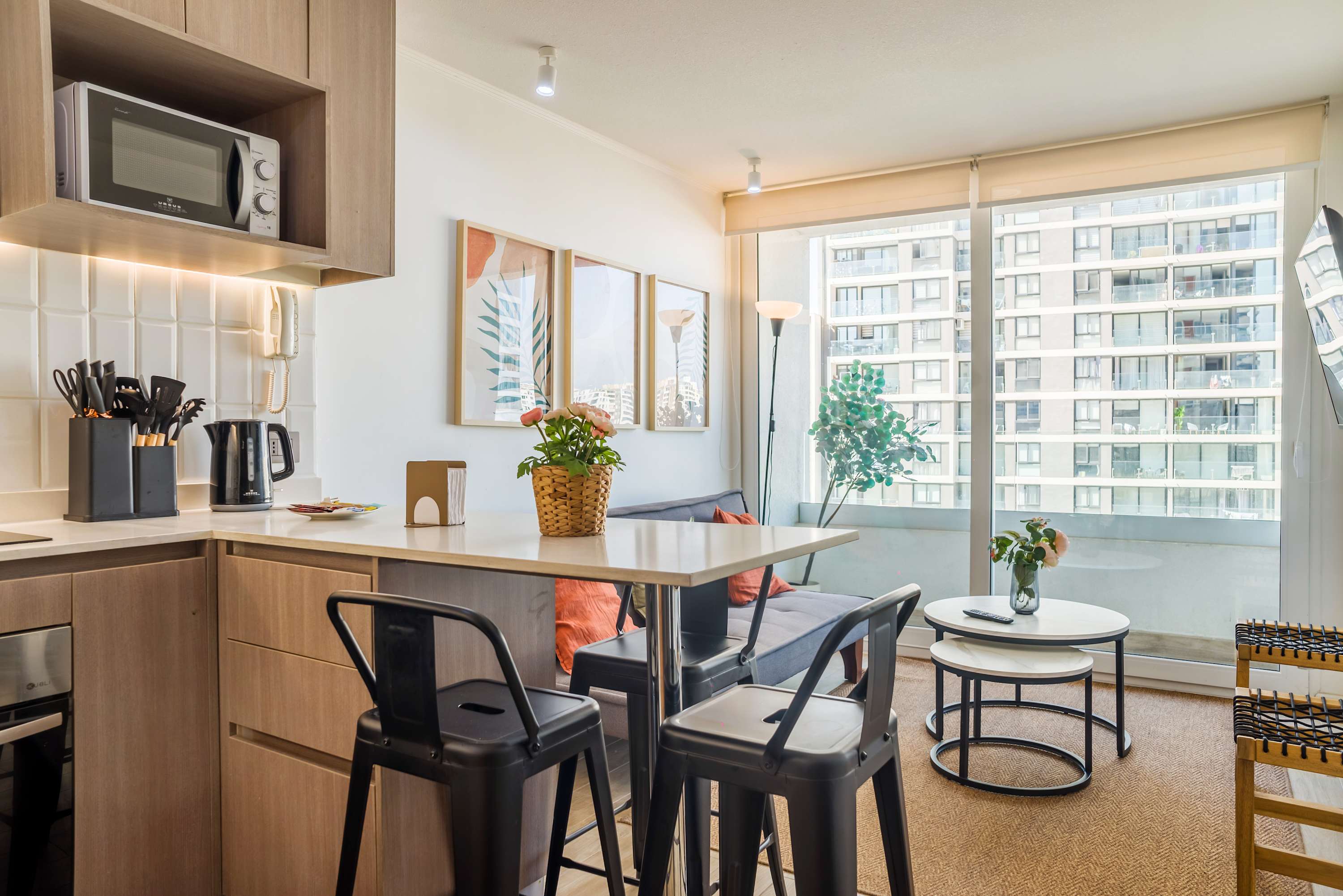 Open-plan kitchen and living area with a breakfast island, botanical artwork, and bright balcony views over the city.