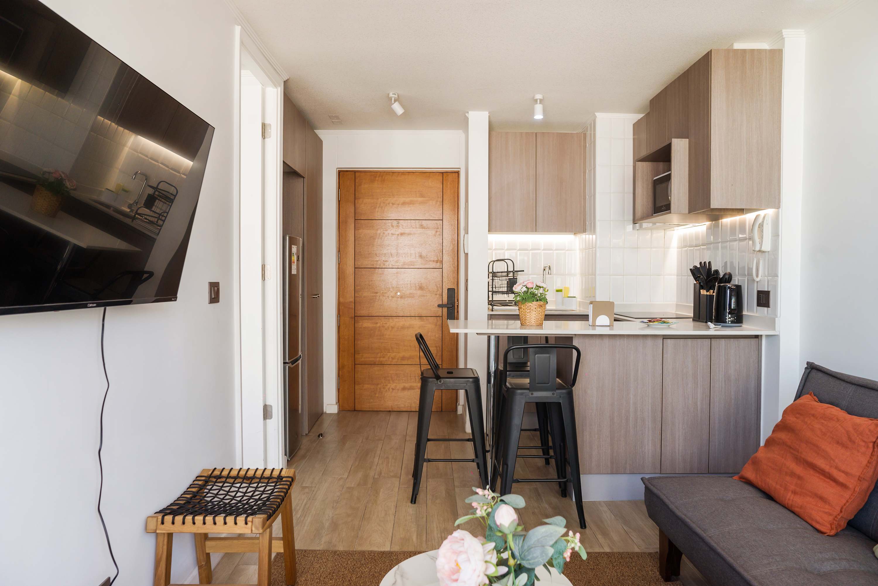 Open-plan studio living area with a gray sofa, orange accents, and a well-equipped kitchen with a convenient breakfast bar.