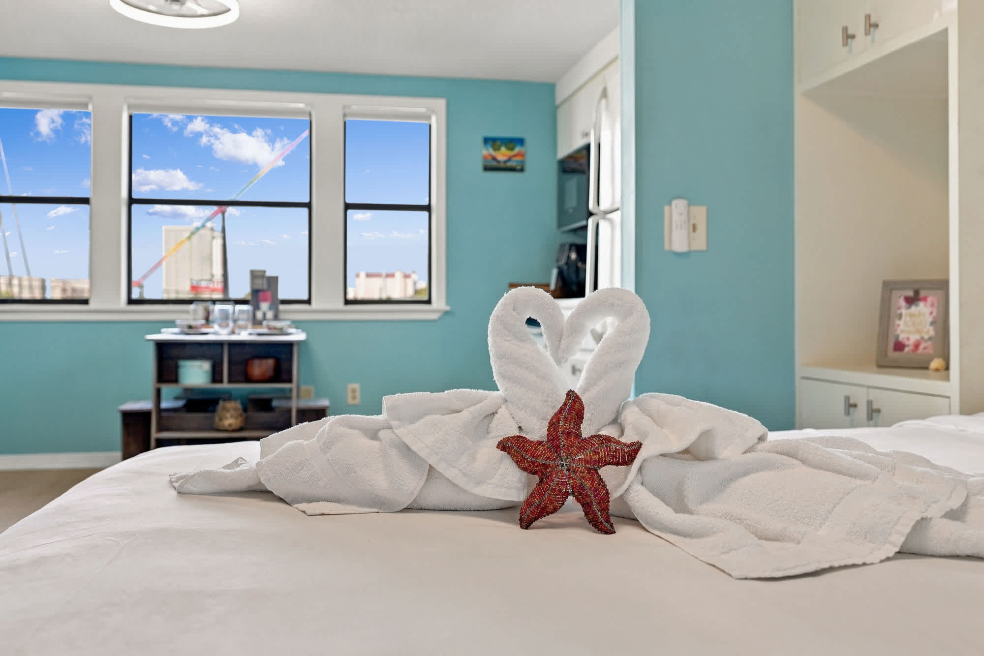 St Thomas SQ 1209C – Bright bedroom with a towel swan display, starfish accent, and windows offering a sky view.
