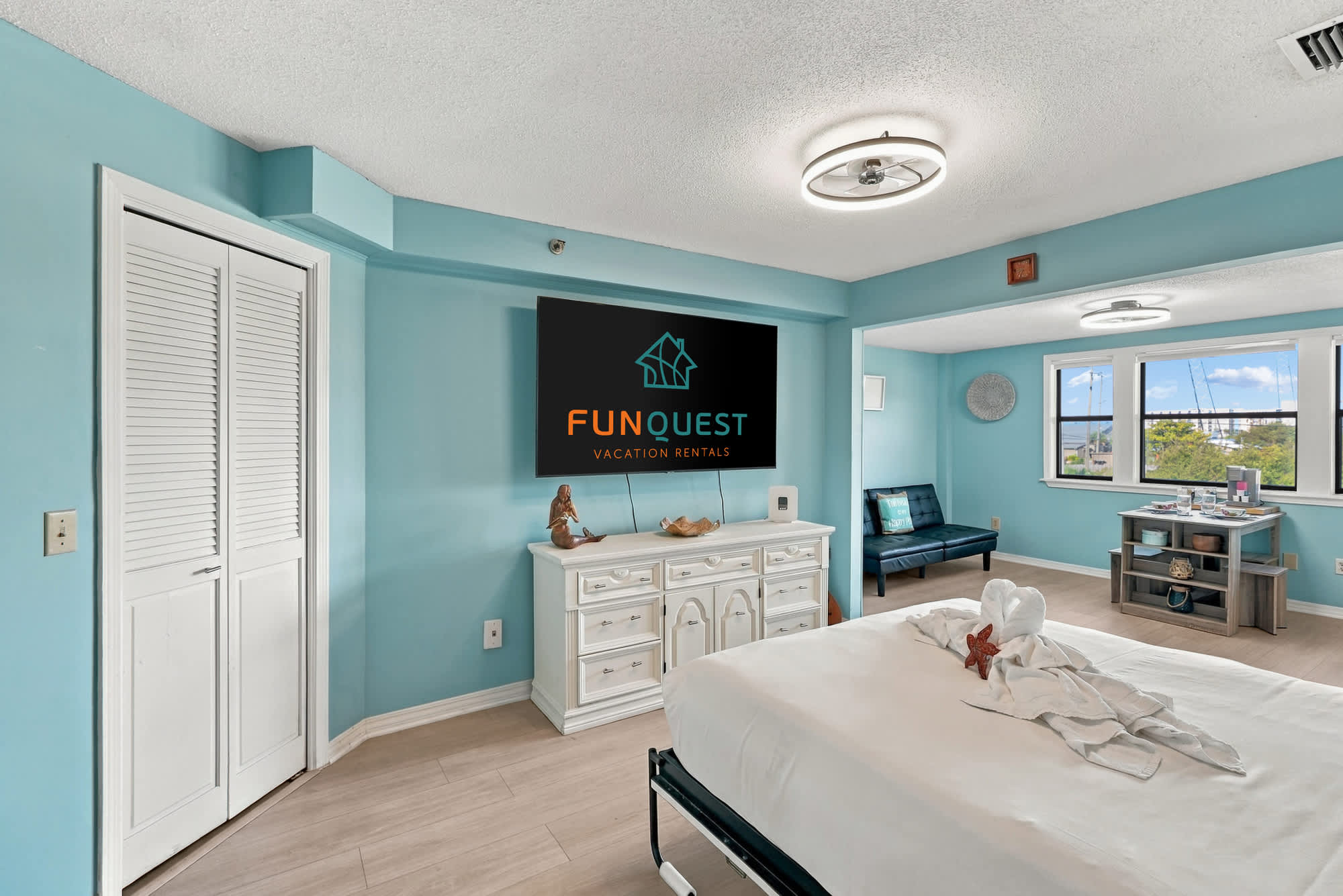 St Thomas SQ 1209C – Cozy bedroom with aqua walls, queen bed, TV, and seating area by windows.