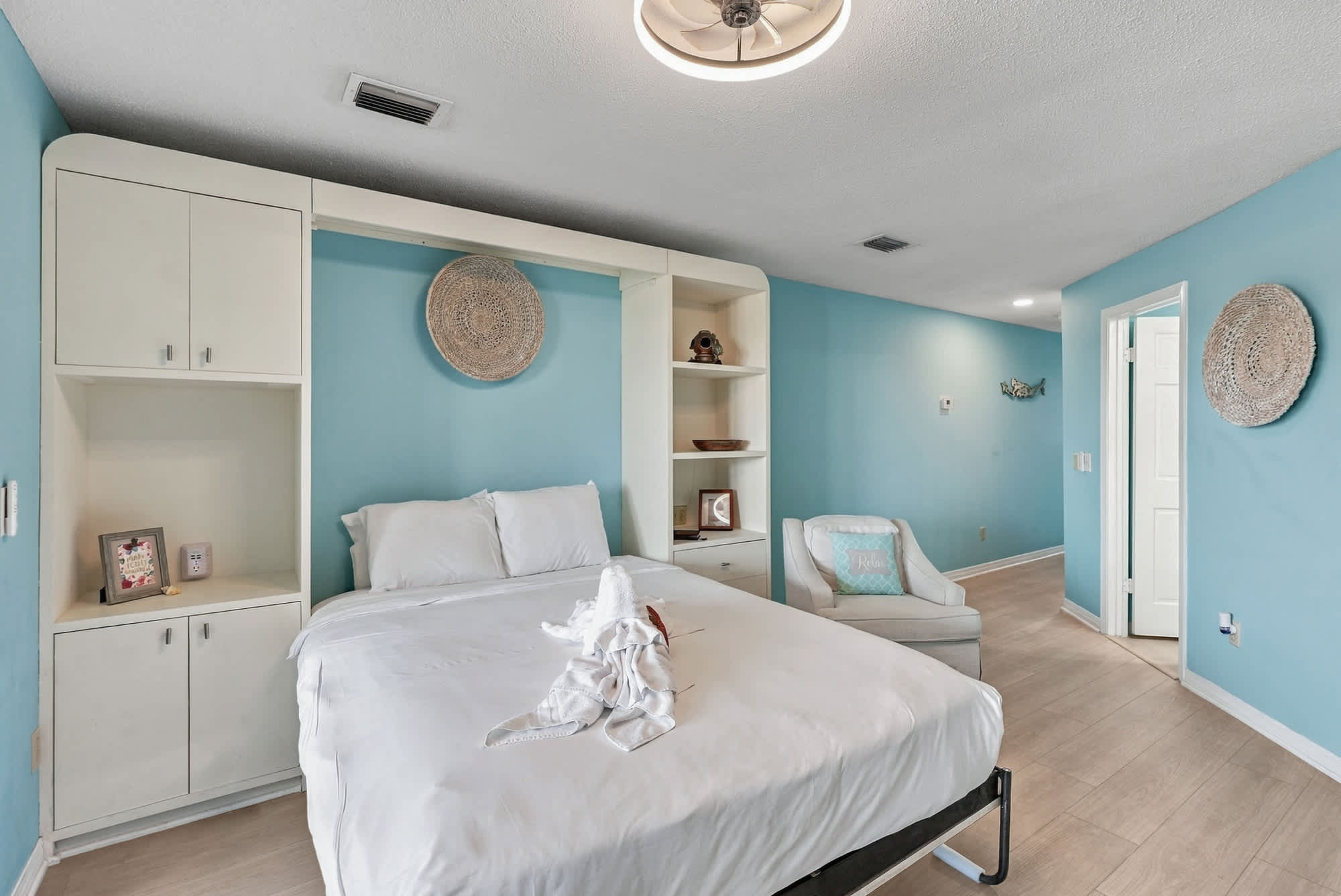St Thomas SQ 1209C – Cozy bedroom with a bed, decorative shelving, light blue walls, and armchair.