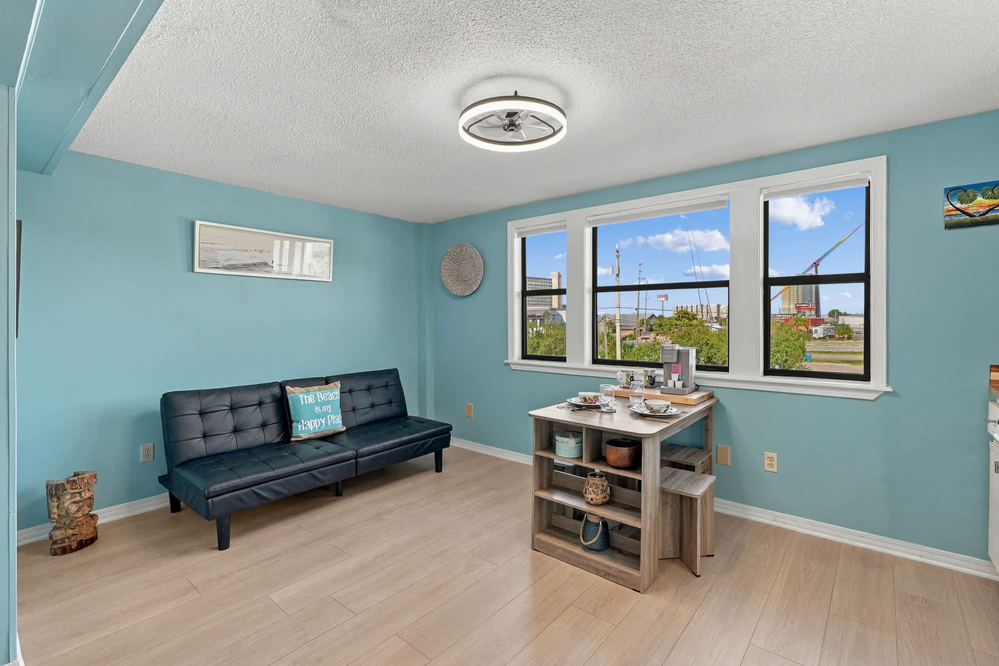 St Thomas SQ 1209C – Bright living area with blue walls, a sofa, dining table, and windows showing a street view.