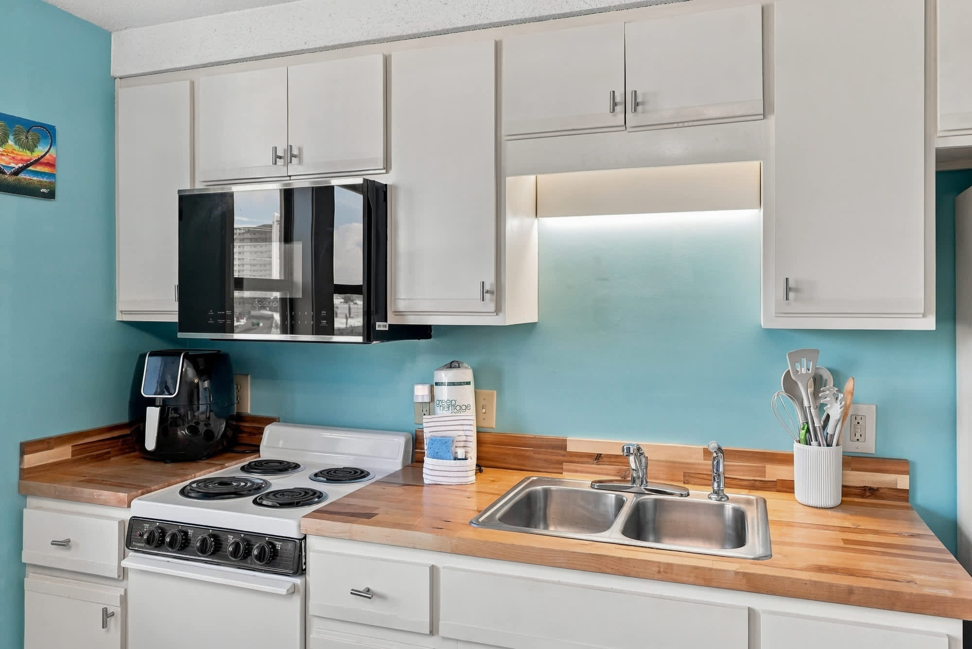 St Thomas SQ 1209C – Modern kitchen with blue wall, white cabinets, stove, sink, and countertop appliances.