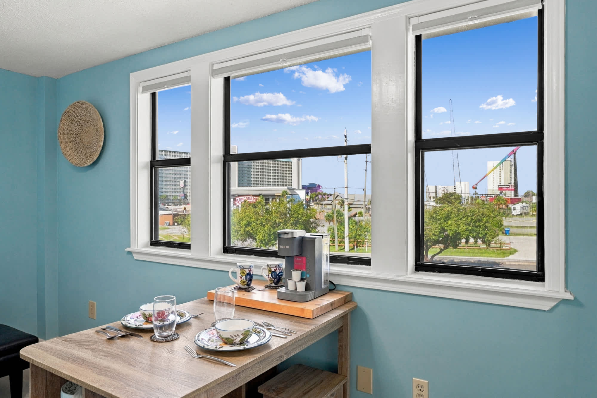 St Thomas SQ 1209C – Dining area with a wooden table, coffee maker, and views of nearby buildings and greenery through large windows.