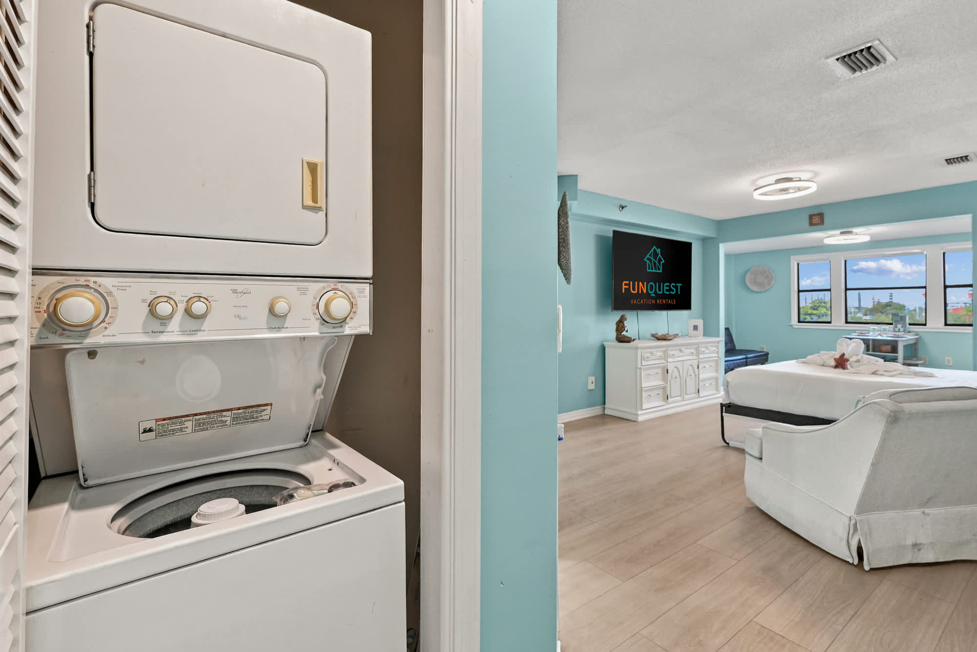 St Thomas SQ 1209C – Washer and dryer unit in a bright studio with a white bed and large windows.