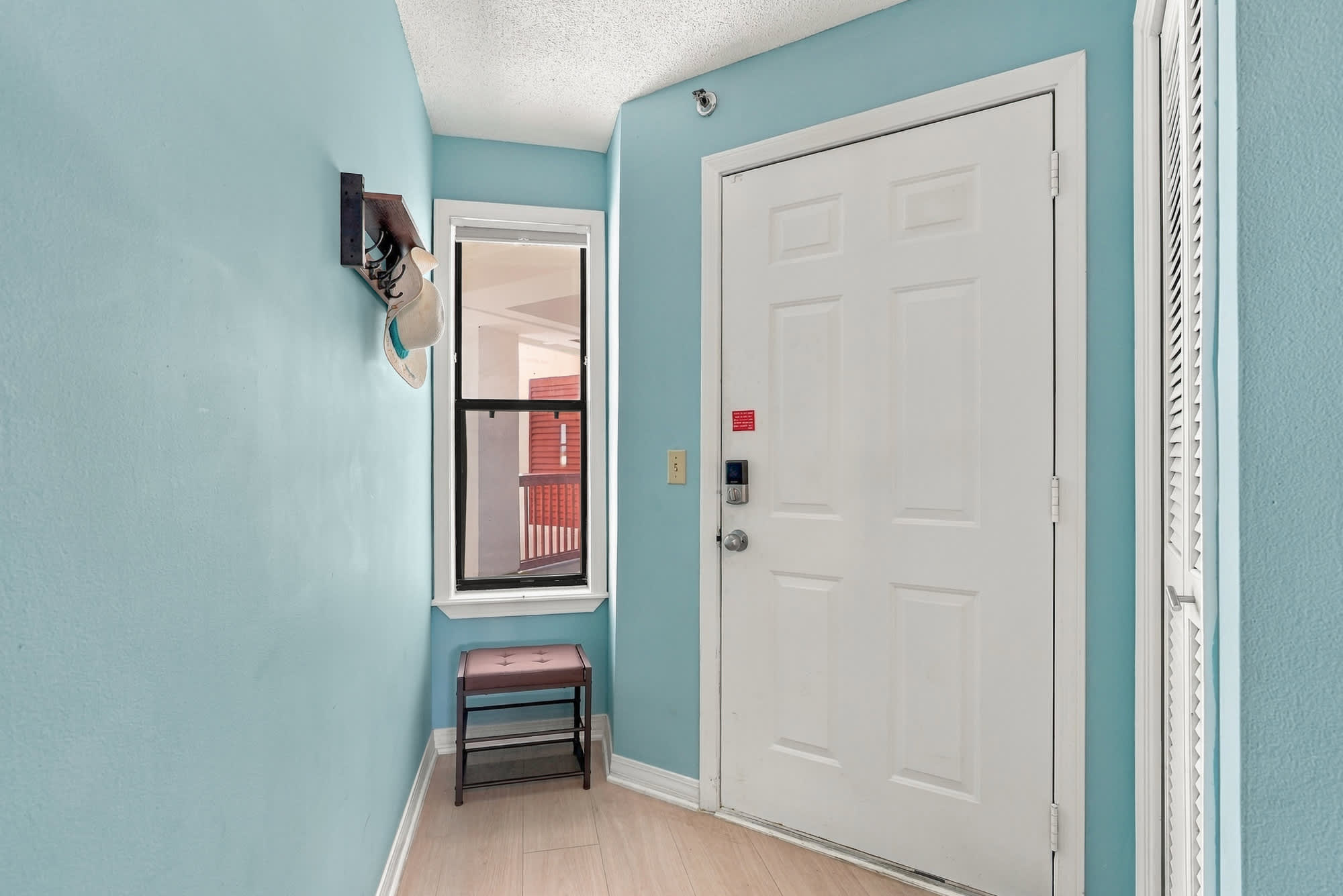 St Thomas SQ 1209C – Bright entryway with turquoise walls, a door, window, and a small brown bench.