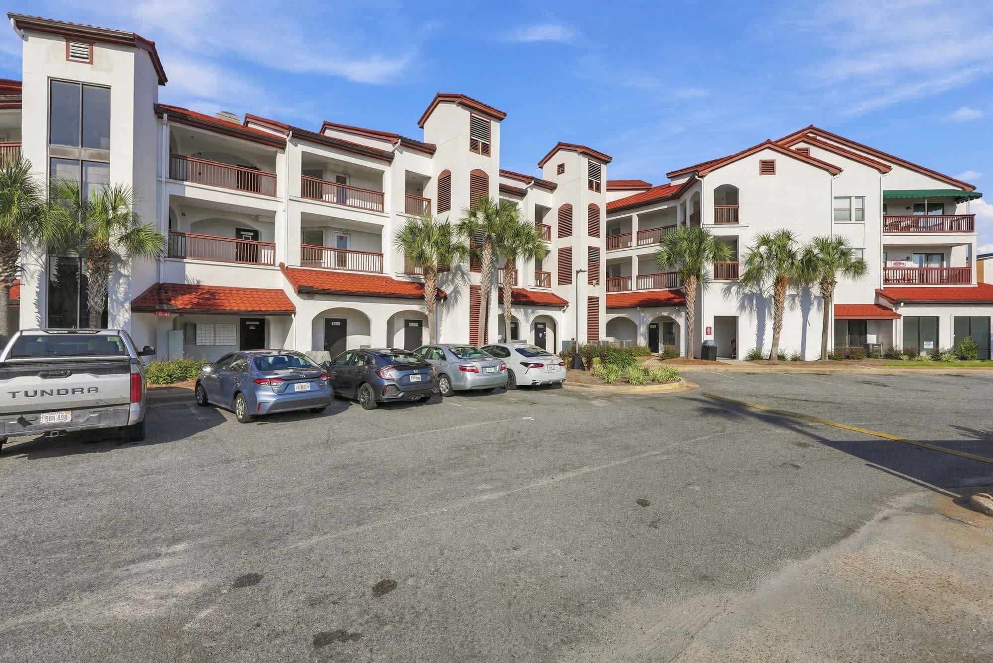 St Thomas SQ 1209C – Three-story building with red tile roof, palm trees, and parked cars in front.