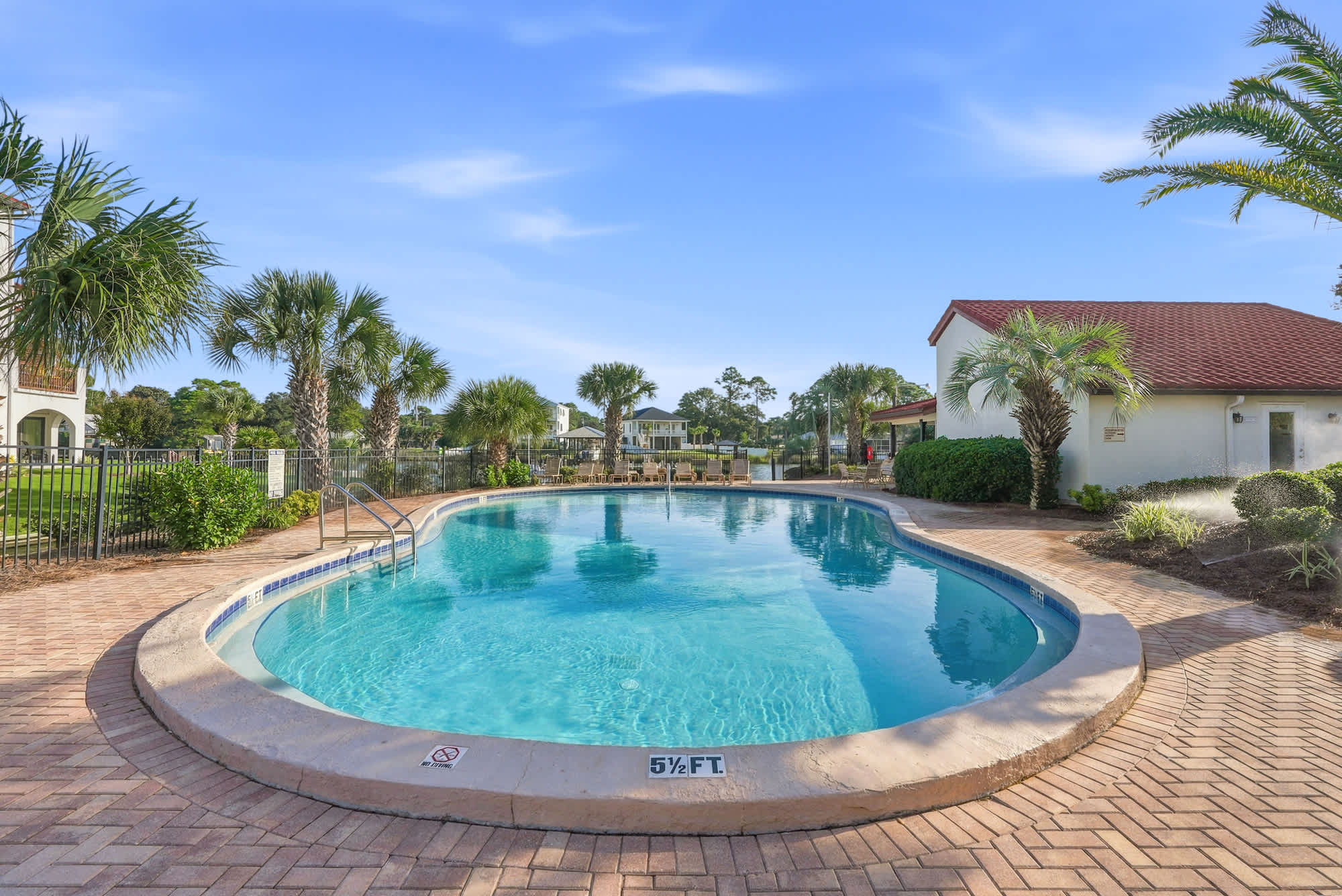 St Thomas SQ 1209C – Swimming pool surrounded by palm trees and paved area, with a residential view in the background.