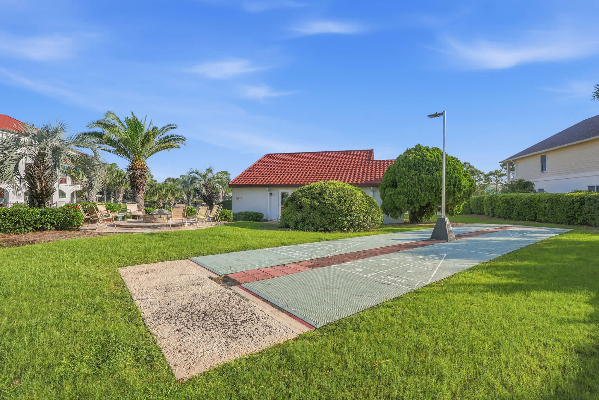 St Thomas SQ 1209C – Grounds with shuffleboard court, palm trees, and seating area near a building with a red roof.